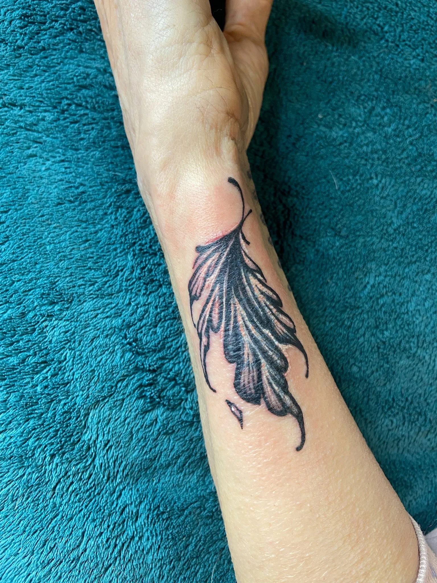 A tattoo of a butterfly on a person's forearm, resting on a teal textured fabric.