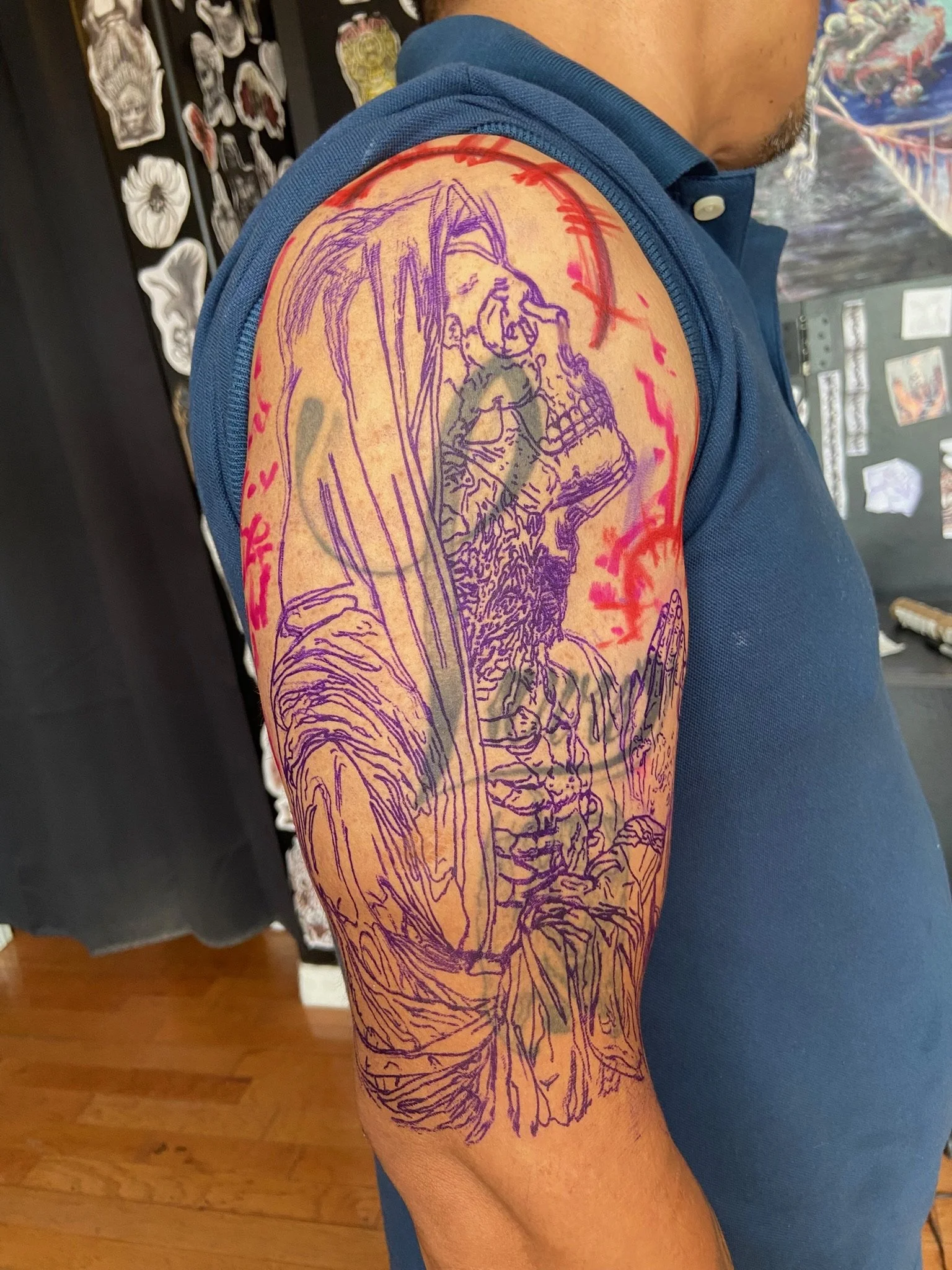 Tattoo of a woman with long hair holding a skull, outlined in purple, with red markings around the upper arm.