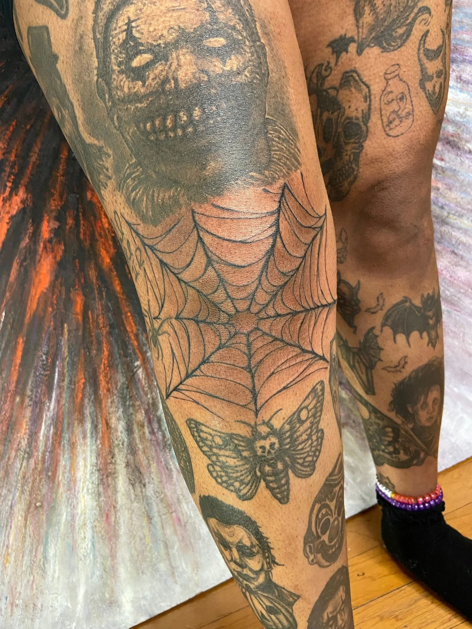 Close-up of a person's arm with multiple tattoos, including a prominent black and gray skull, a spider web, a butterfly, and various other designs.