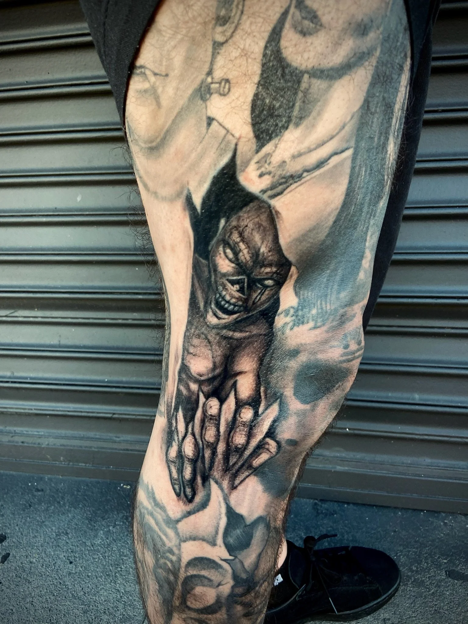 Tattoo on a person's leg depicting a fierce skull with a lidless eye, along with hands holding a sword.