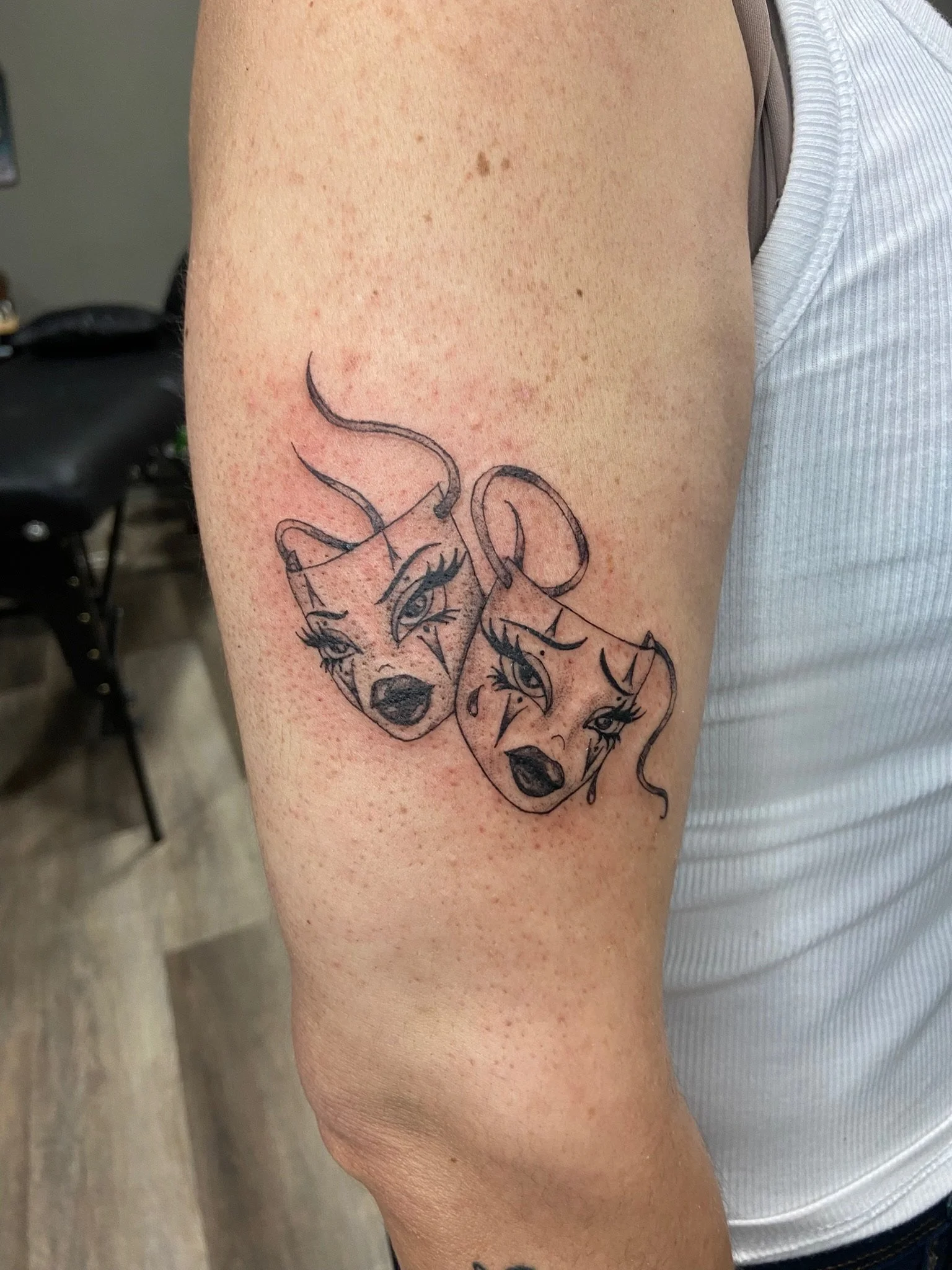Tattoo of three stylized female faces on upper arm.