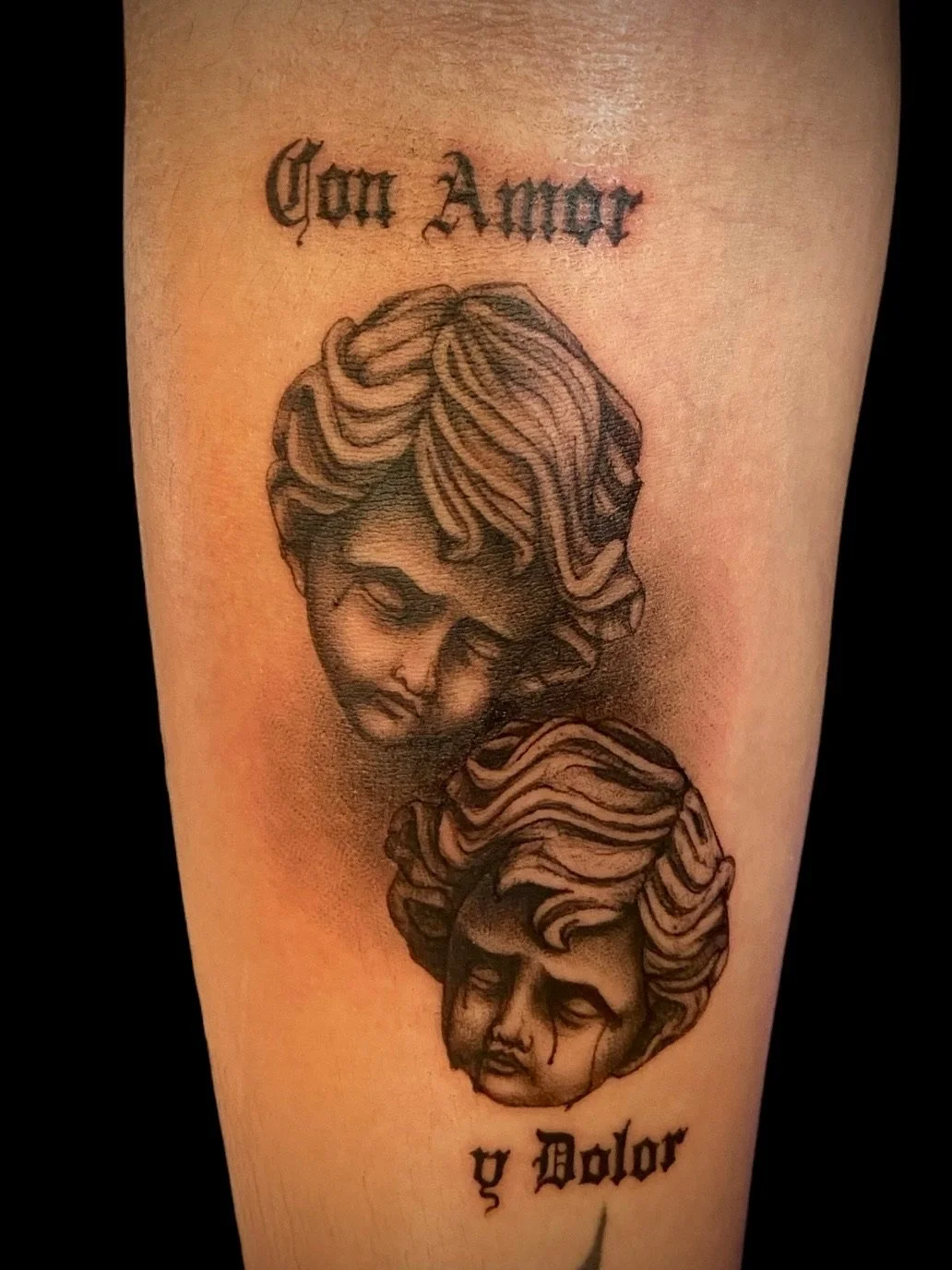 Tattoo of two faces with flowing hair, one above the other, with Italian text "Con Amore" at the top and "y Dolor" at the bottom.