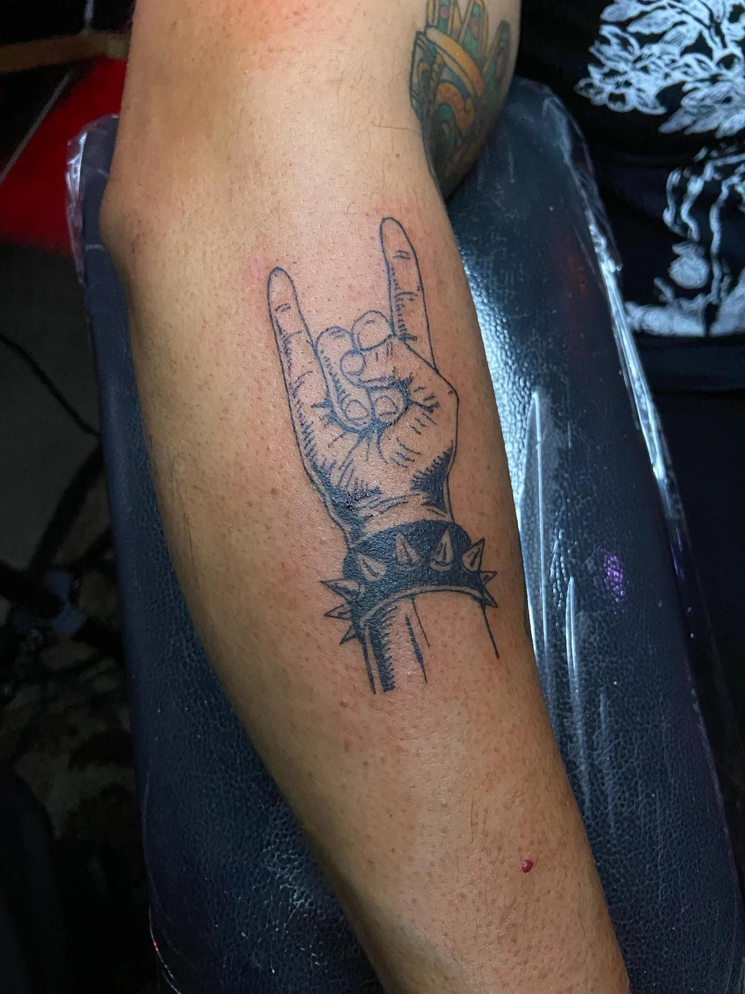 Tattoo of a hand with fingers making a middle finger gesture, surrounded by spiked embellishments, on a person's arm.