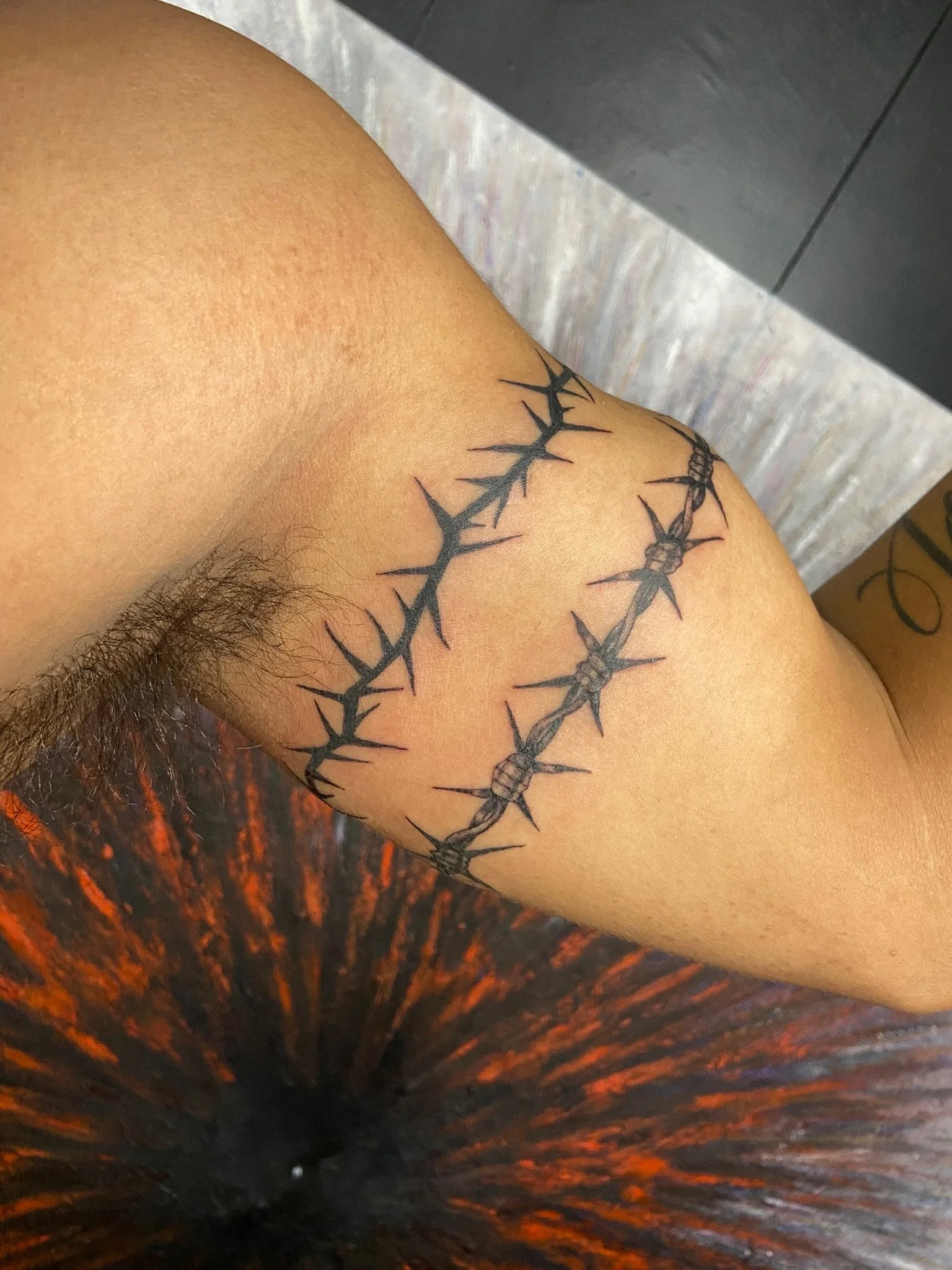 Close-up of a person's shoulder with a black tattoo resembling barbed wire or a thorny vine.