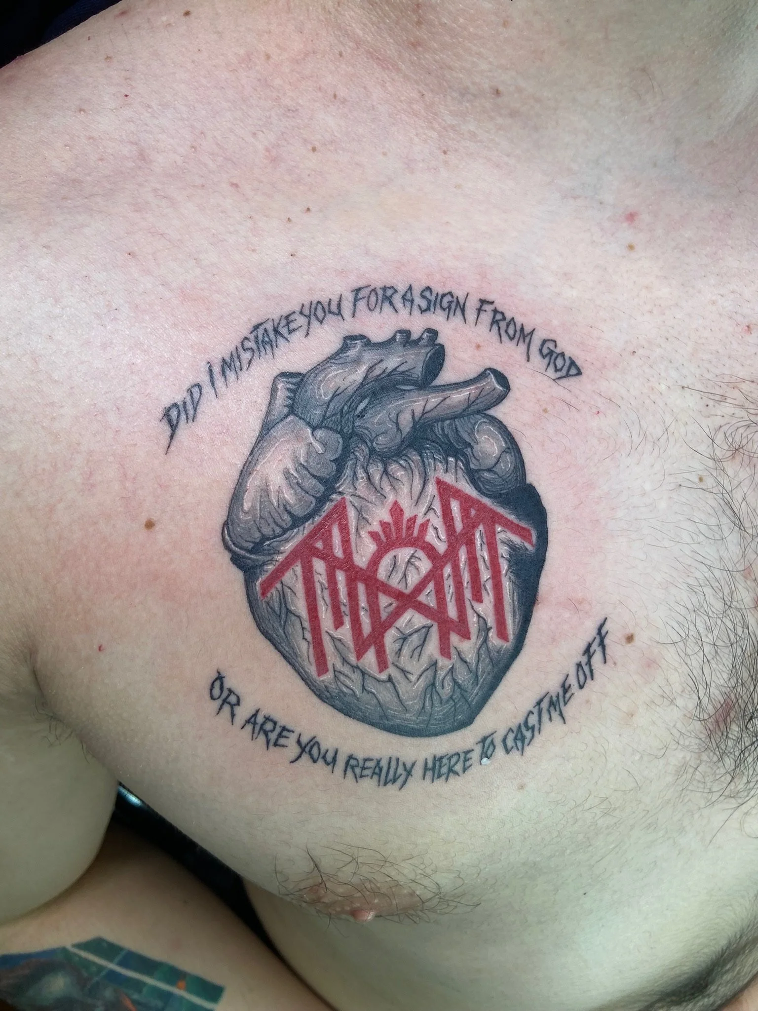 Tattoo of a realistic anatomical heart with text above and below it. The text reads: "Did I mistake you for a sign from God" above and "or are you really here to cast me out?" below.
