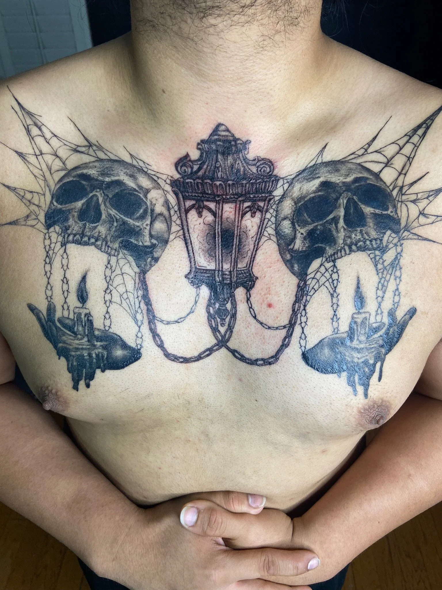 Tattoo of two skulls with a chandelier and spiderweb design tattooed across the chest.