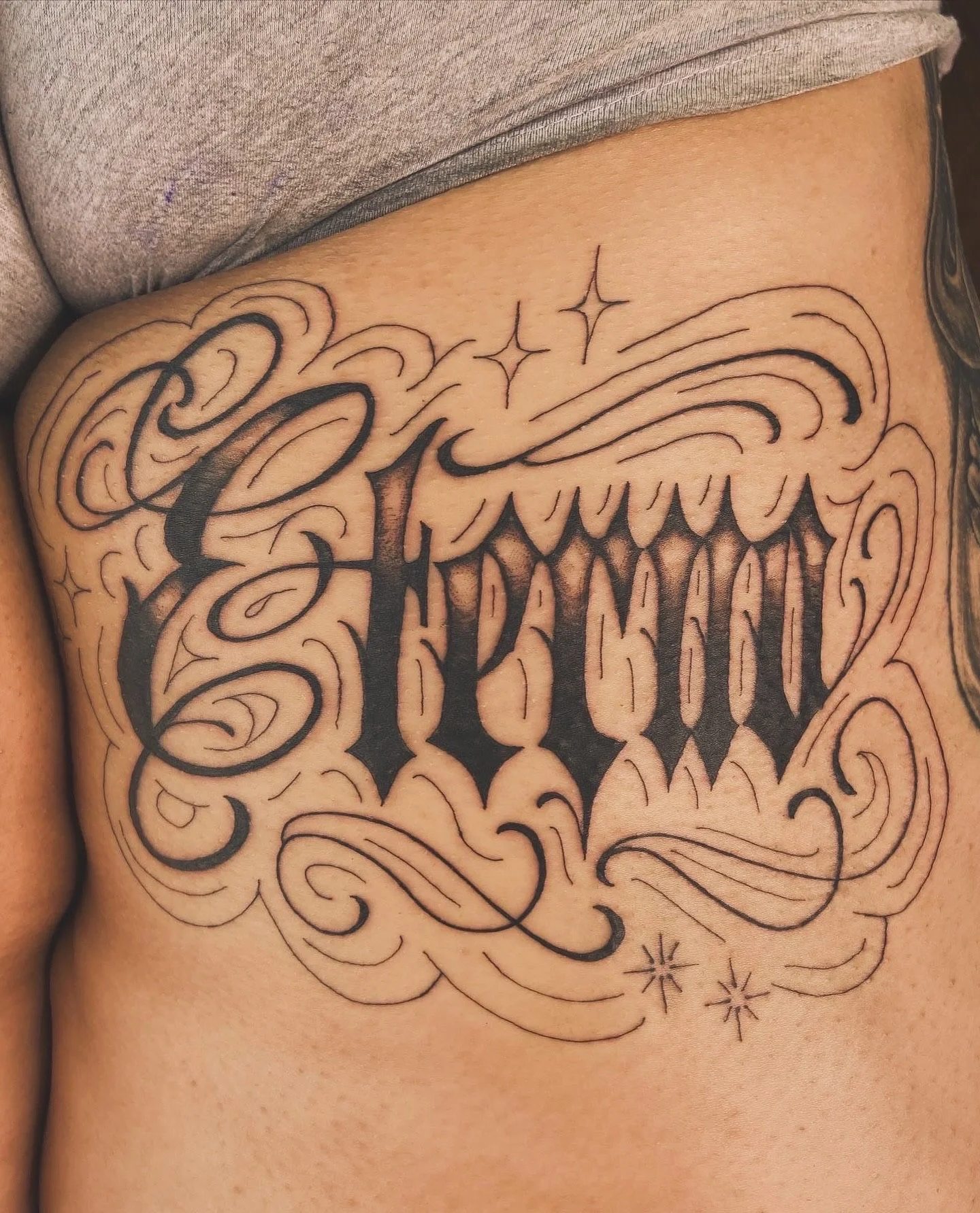 A tattoo with ornate script and decorative elements on a person's side.