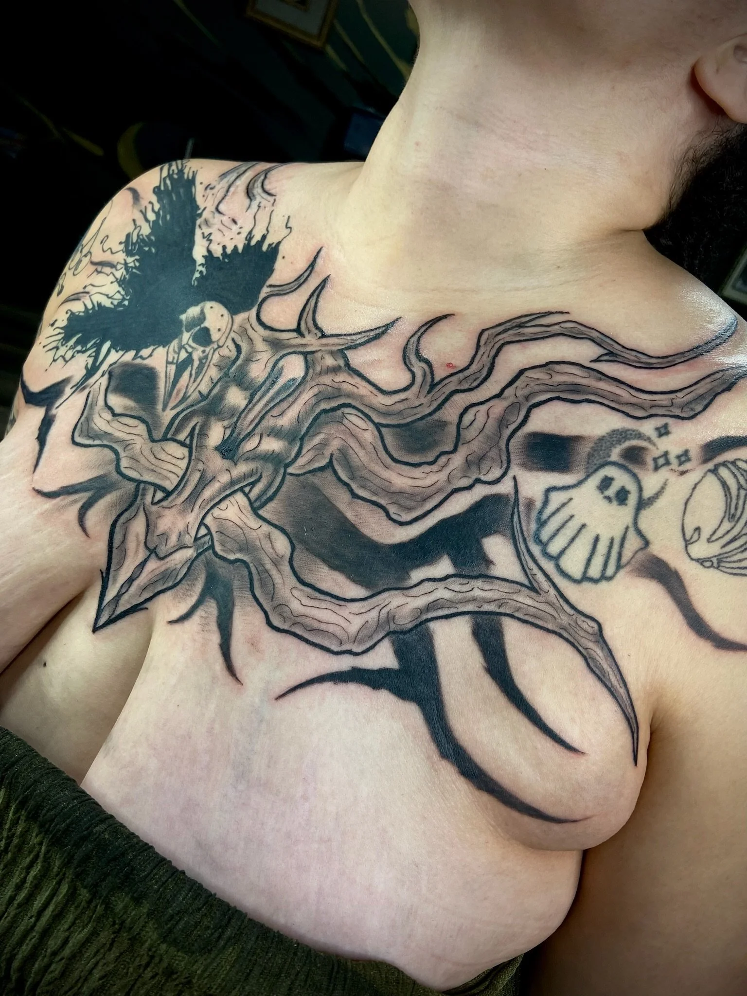 A person with a large, dark tattoo of a bird with outstretched wings on their shoulder and upper chest, along with other black ink designs.
