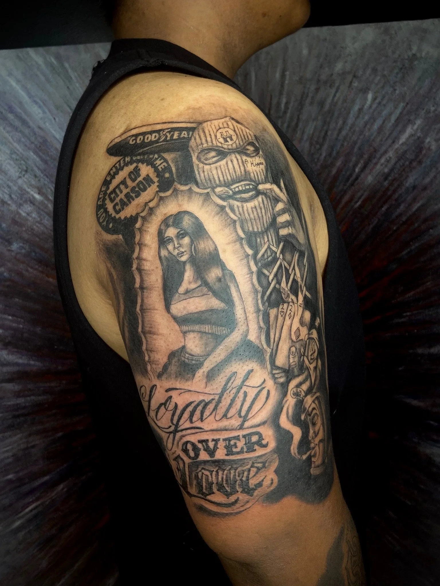 Tattoo of a woman, a skull wearing a beanie, a chain, a police badge with the words 'CITY OF CARSON,' and various decorative elements and text on the person's arm.