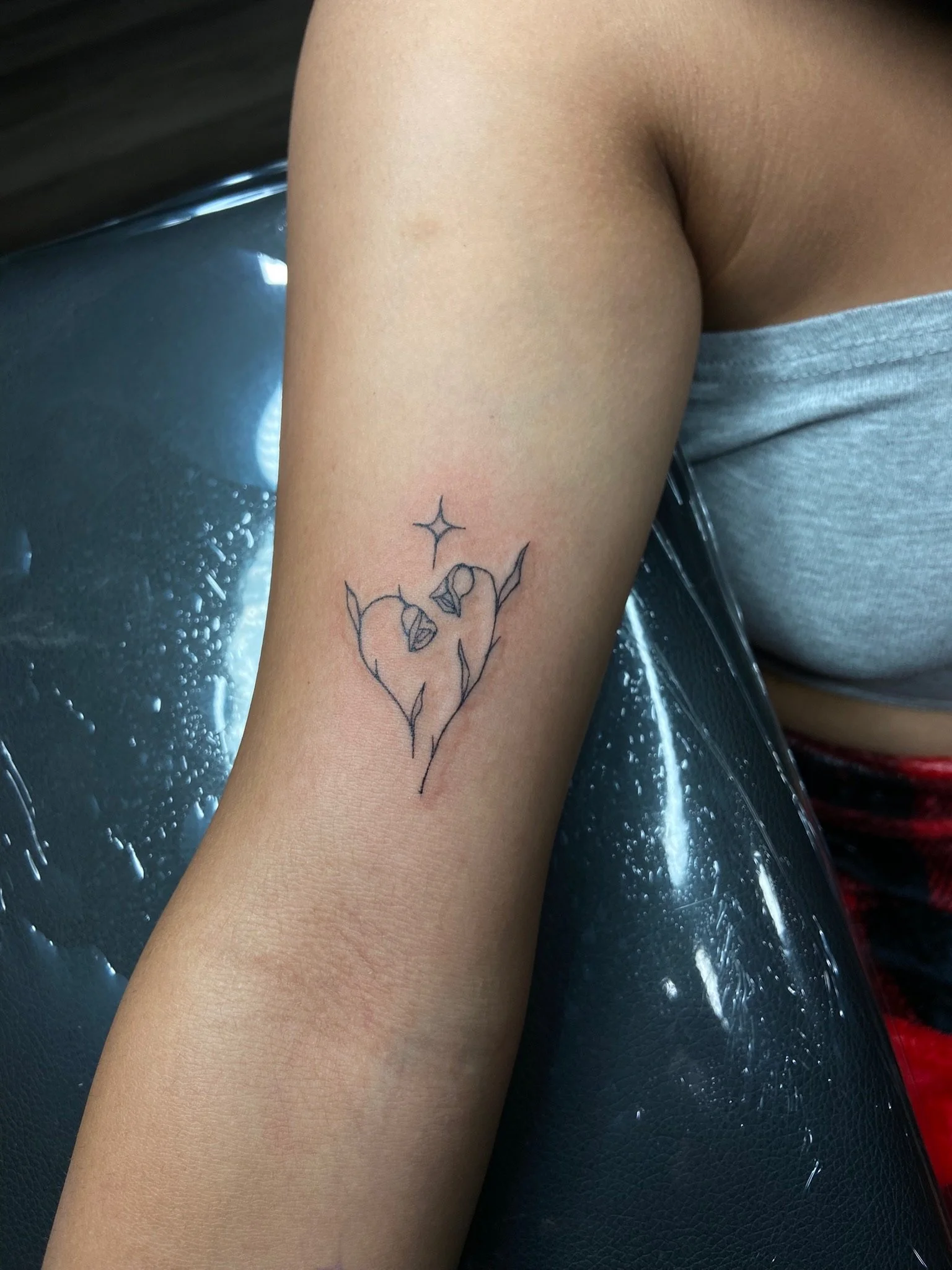 A person's arm with a tattoo of a stylized heart with a star above it, seen against a dark surface.