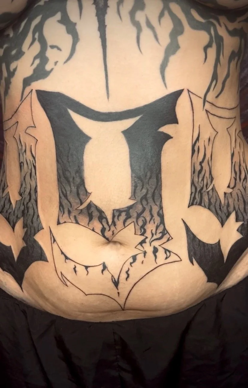 Tattoo of a bat with flames around it on a person's abdomen.