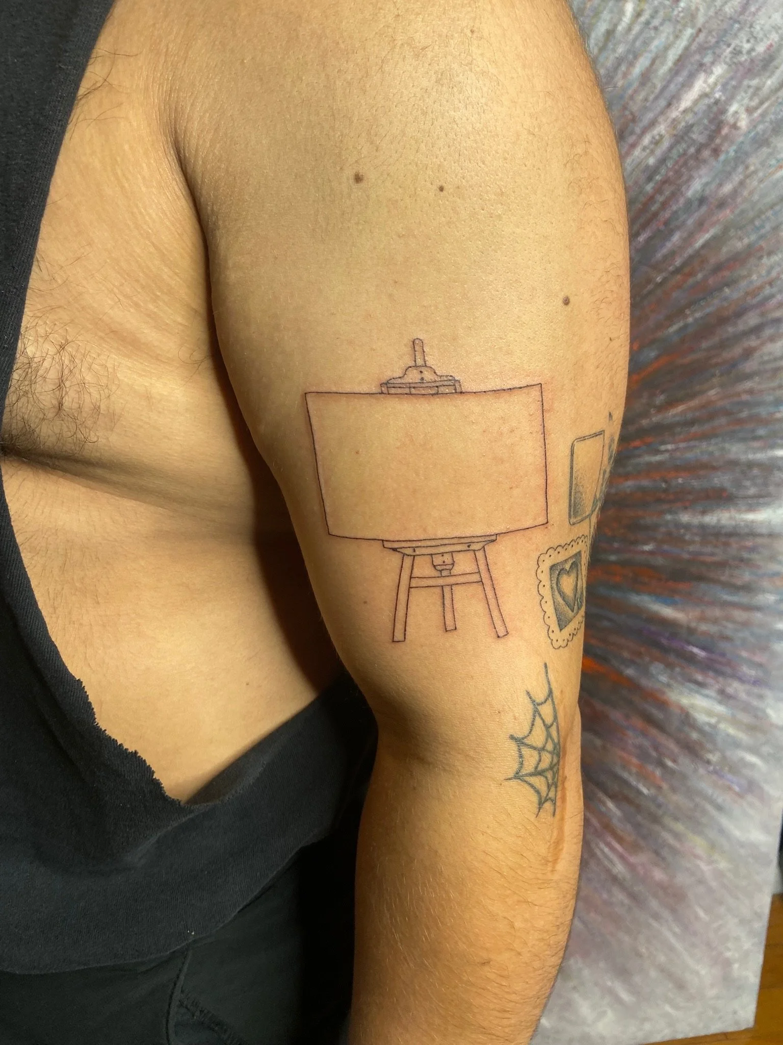 Close-up of a person's upper arm with a tattoo of a camera and a spider web tattoo on the lower arm.