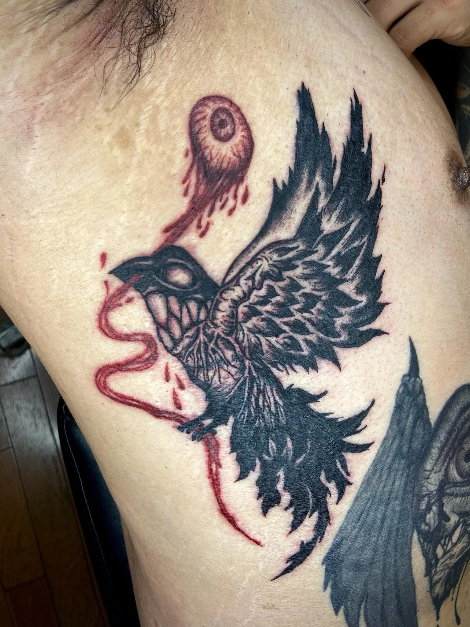 Tattoo of a black and gray dragon with a red eye and a red tongue on a person's upper arm.