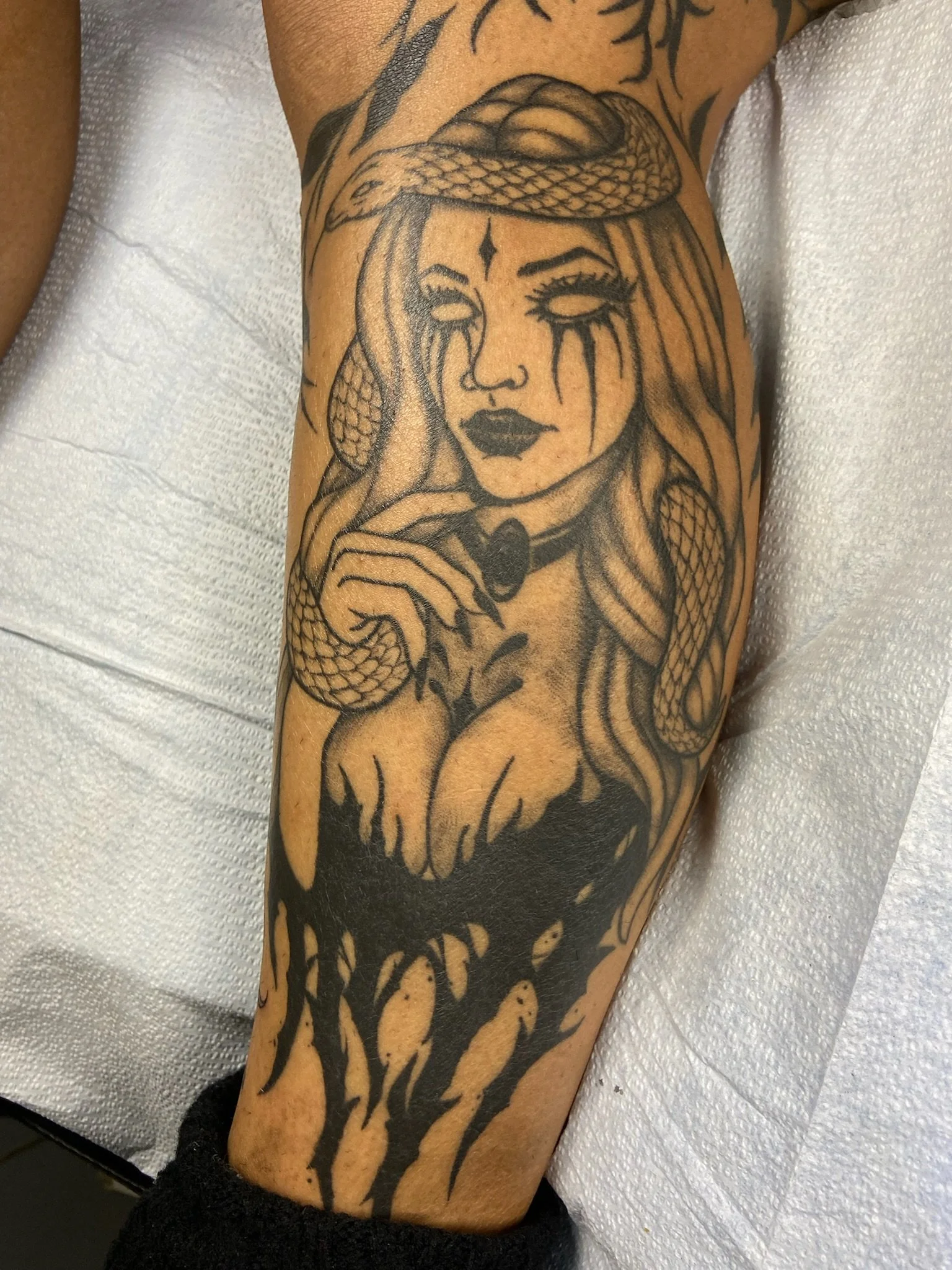 Tattoo of a woman with a serpent on her head and black makeup. Blackwork and color.