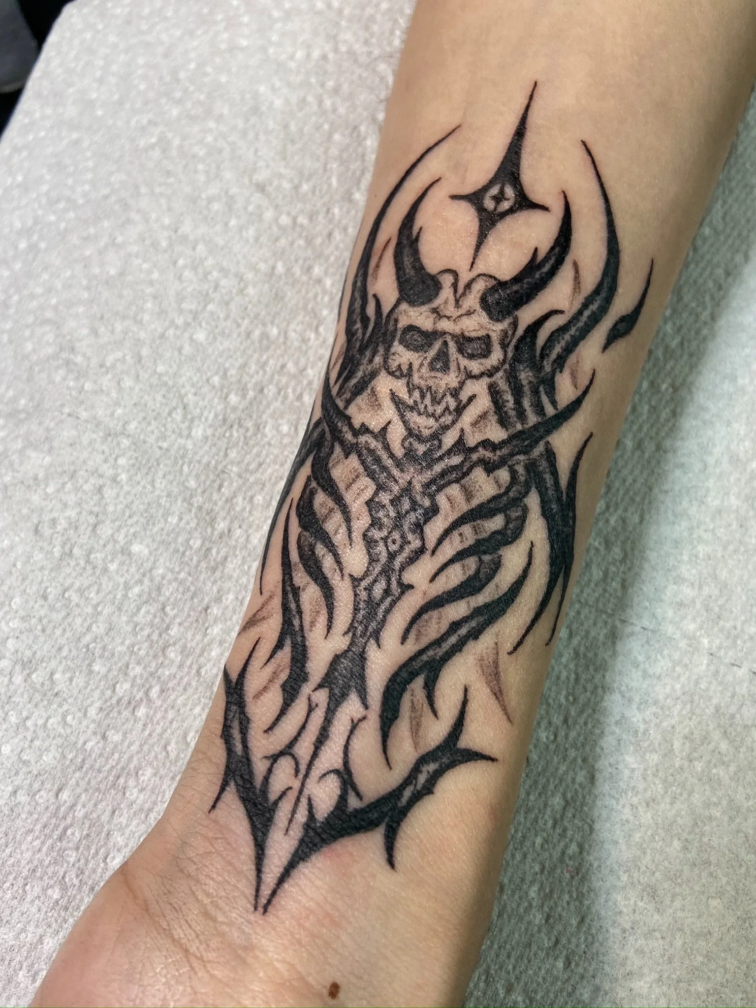 Tattoo of a skull with flames on a person's forearm.