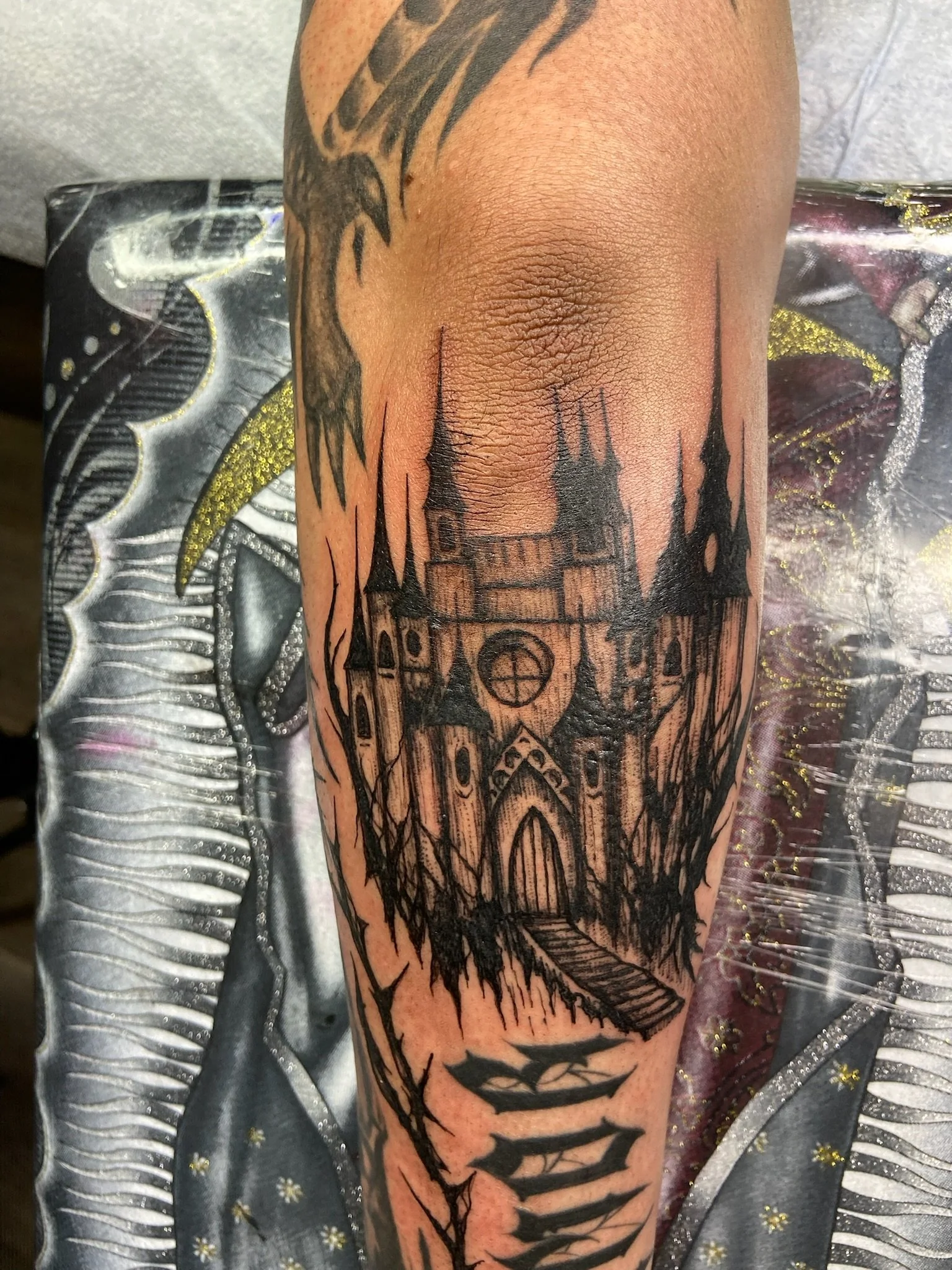 Tattoo of a haunted house silhouette with trees on a person's arm in the style of blackwork.