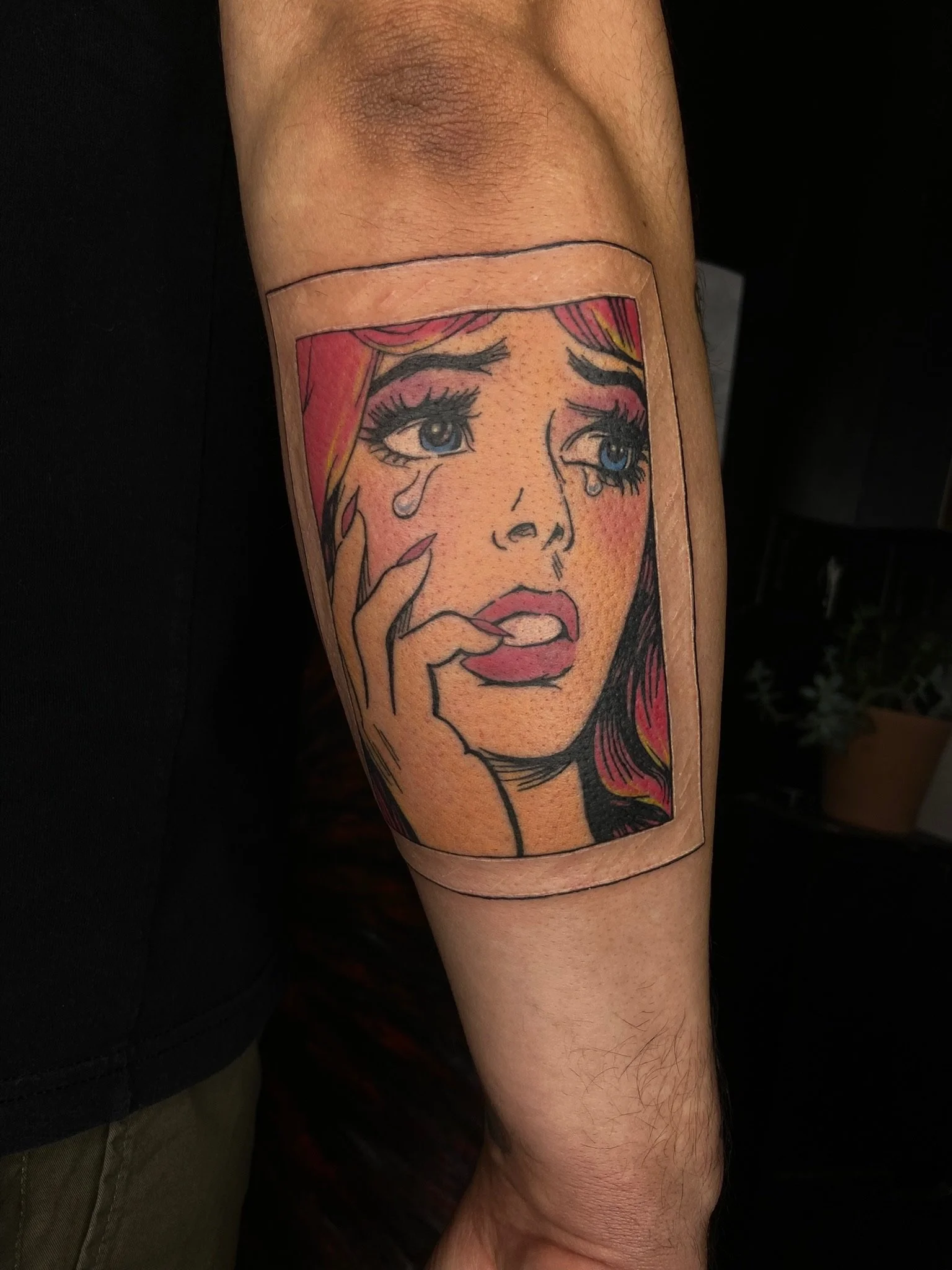 Close-up of a colorful tattoo of a woman with tears on her cheek, detailed with bold lines and vibrant colors, on a person's arm.