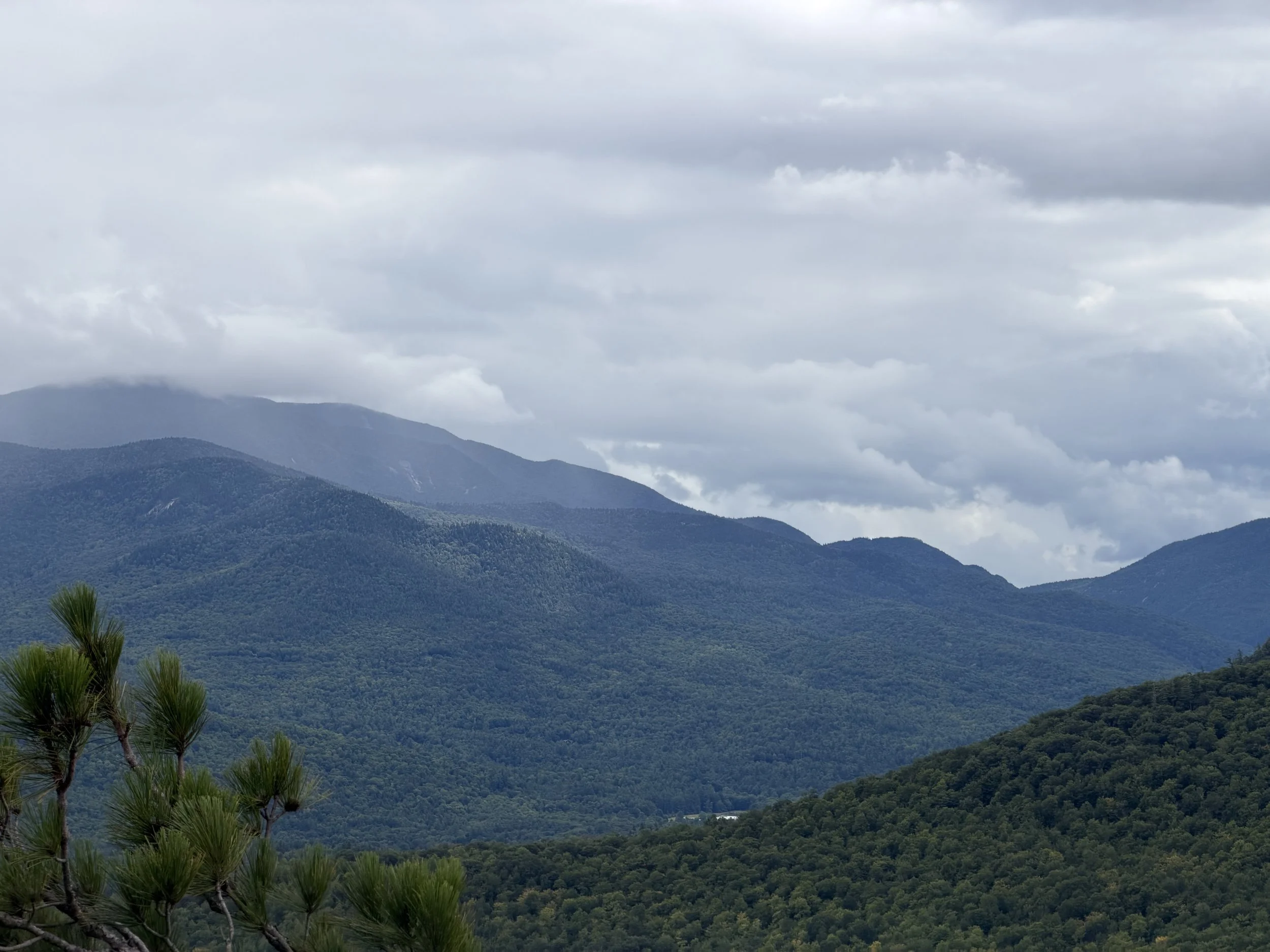 Mountain range with forested slopes, cloudy sky with gray clouds.