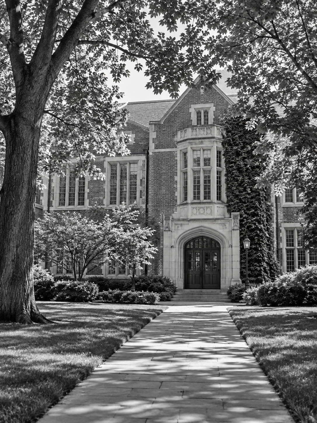 A large brick house with a grand entrance, surrounded by trees and well-maintained landscaping, black and white photo.