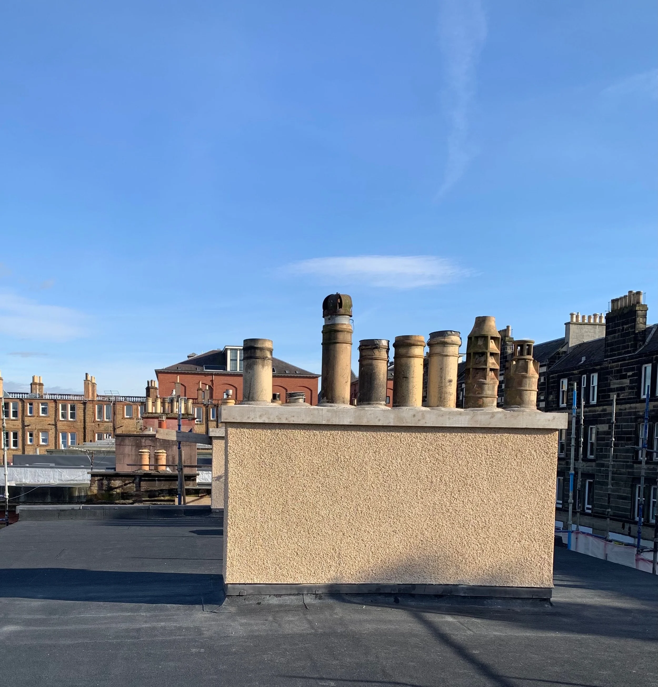 A building rooftop with multiple brick chimneys against a clear blue sky.