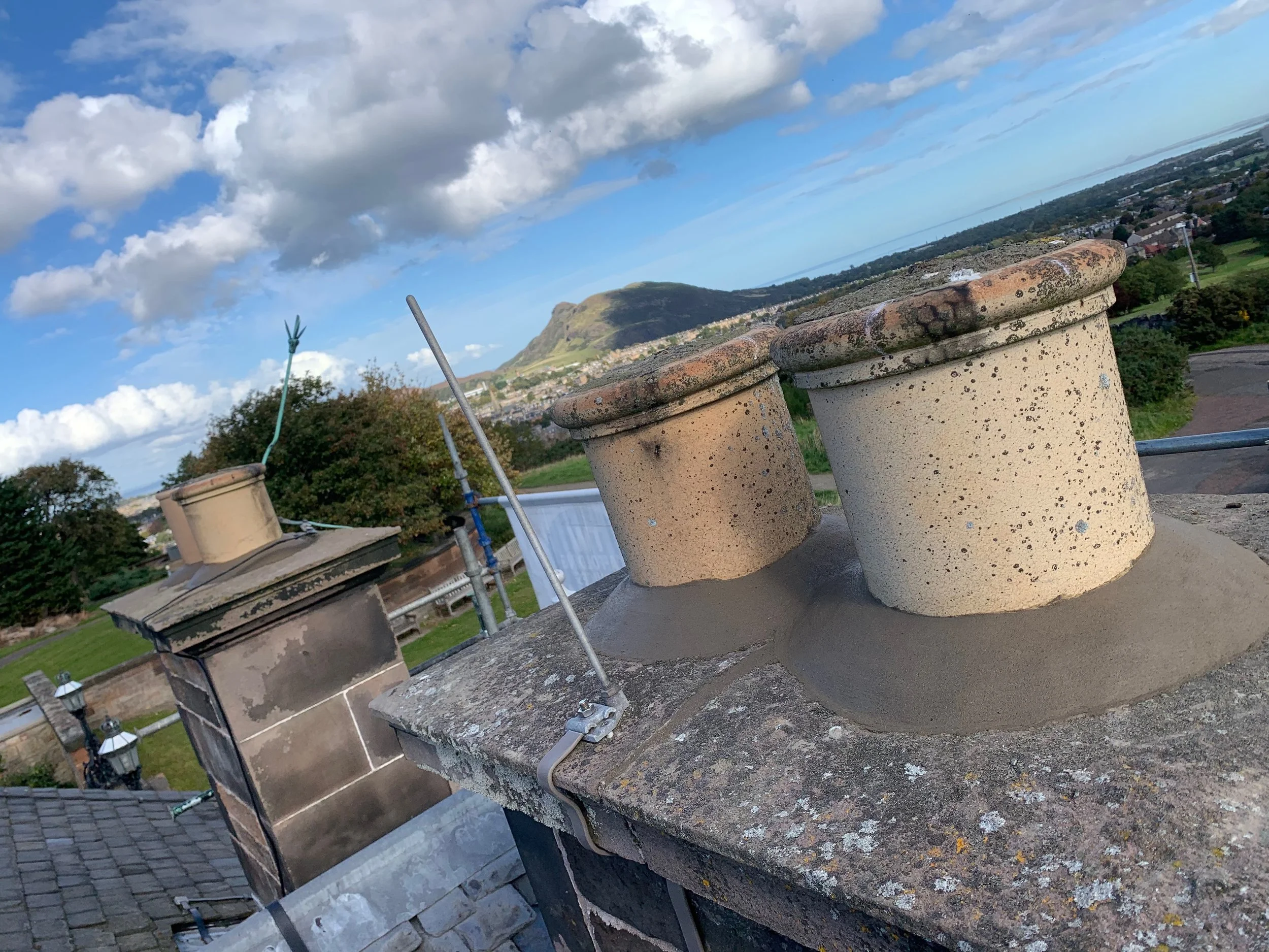 Multiple rooftop chimneys and vents on a building with a mountain in the background under a partly cloudy sky.