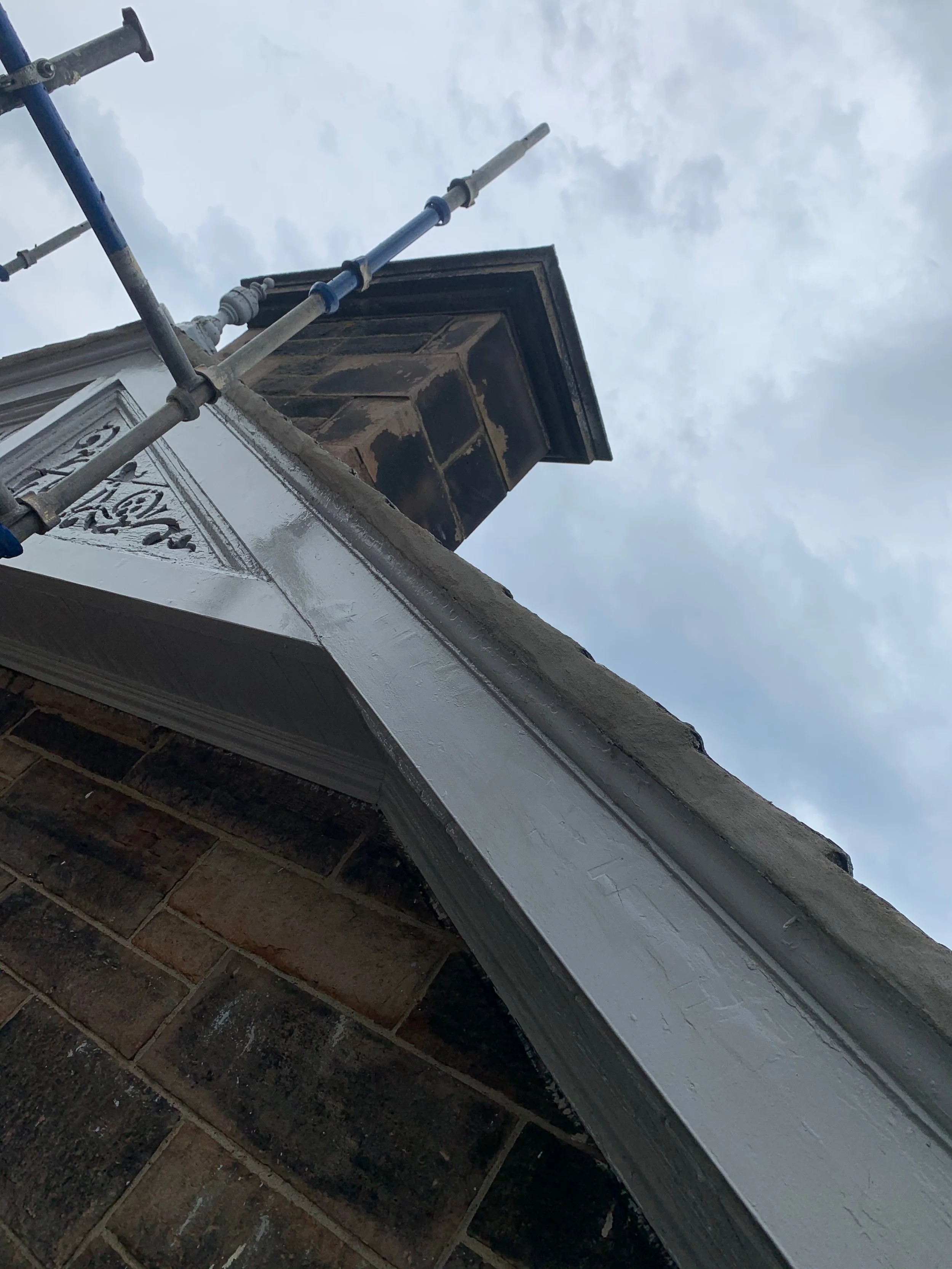 A close-up of a chimney on a brick building, with scaffolding next to it, against a cloudy sky.