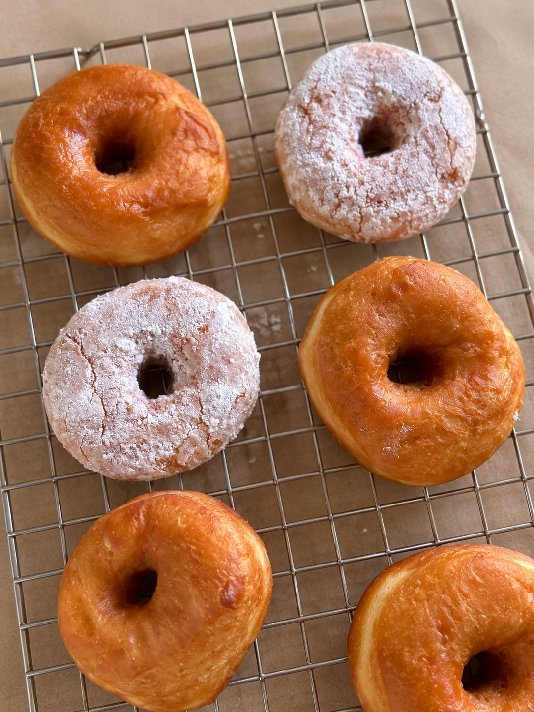 Six glazed and powdered donuts cooling on a wire rack.