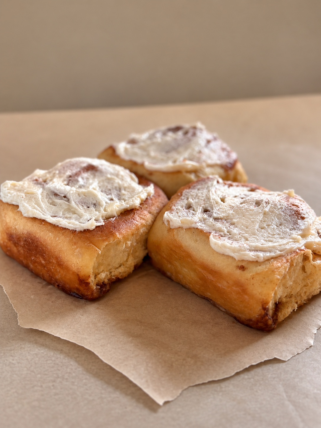 Three cinnamon rolls with white creamy frosting on top, on brown parchment paper.
