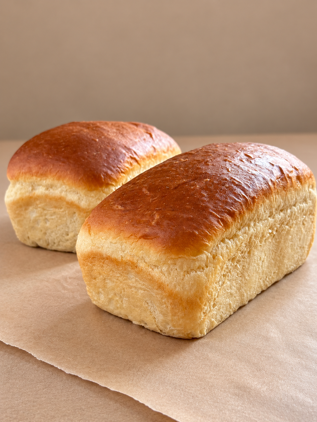 Two loaves of freshly baked bread with golden brown crust, placed on a piece of parchment paper.