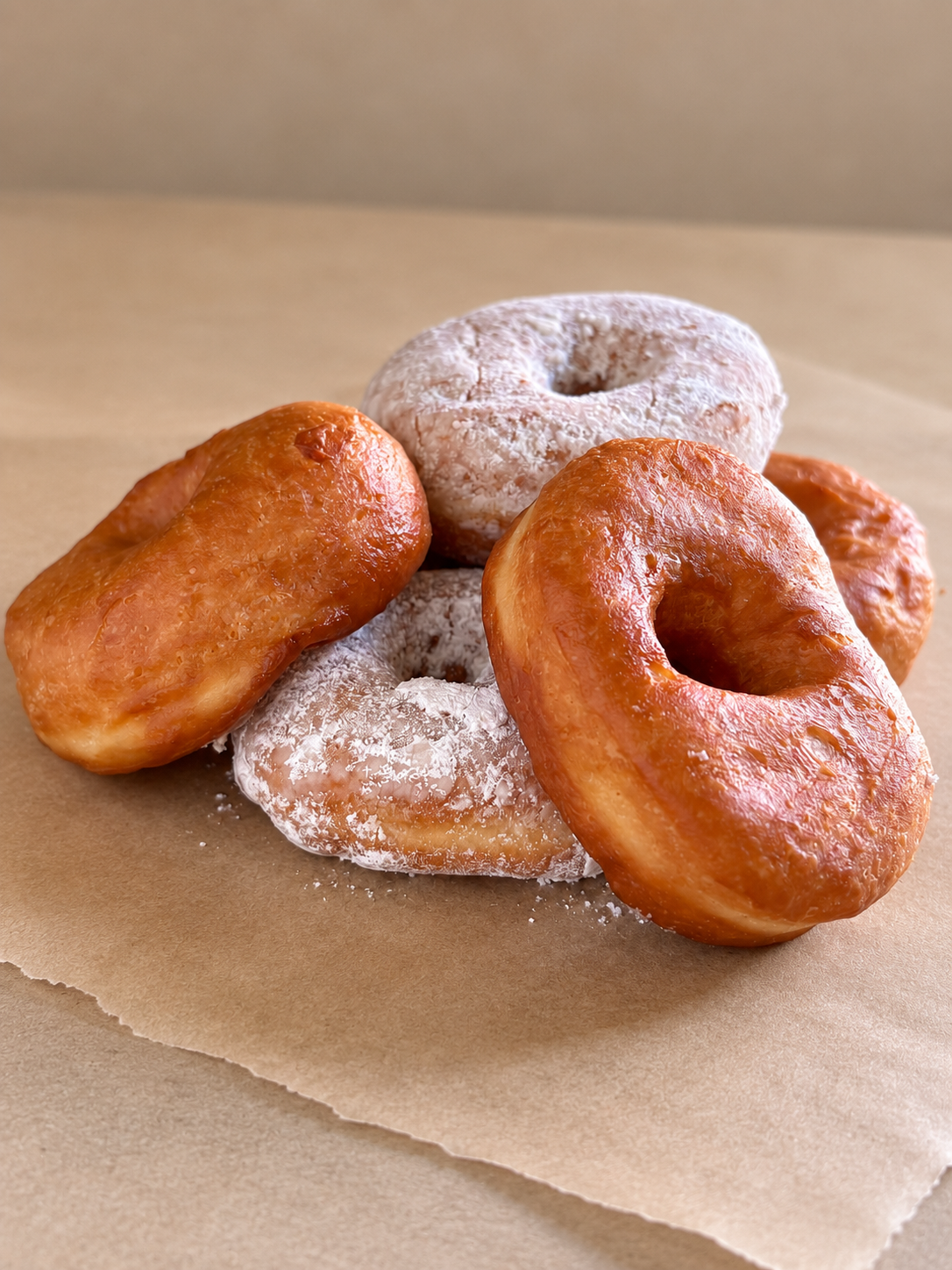 Assorted donuts, some glazed and some dusted with powdered sugar, on brown parchment paper.