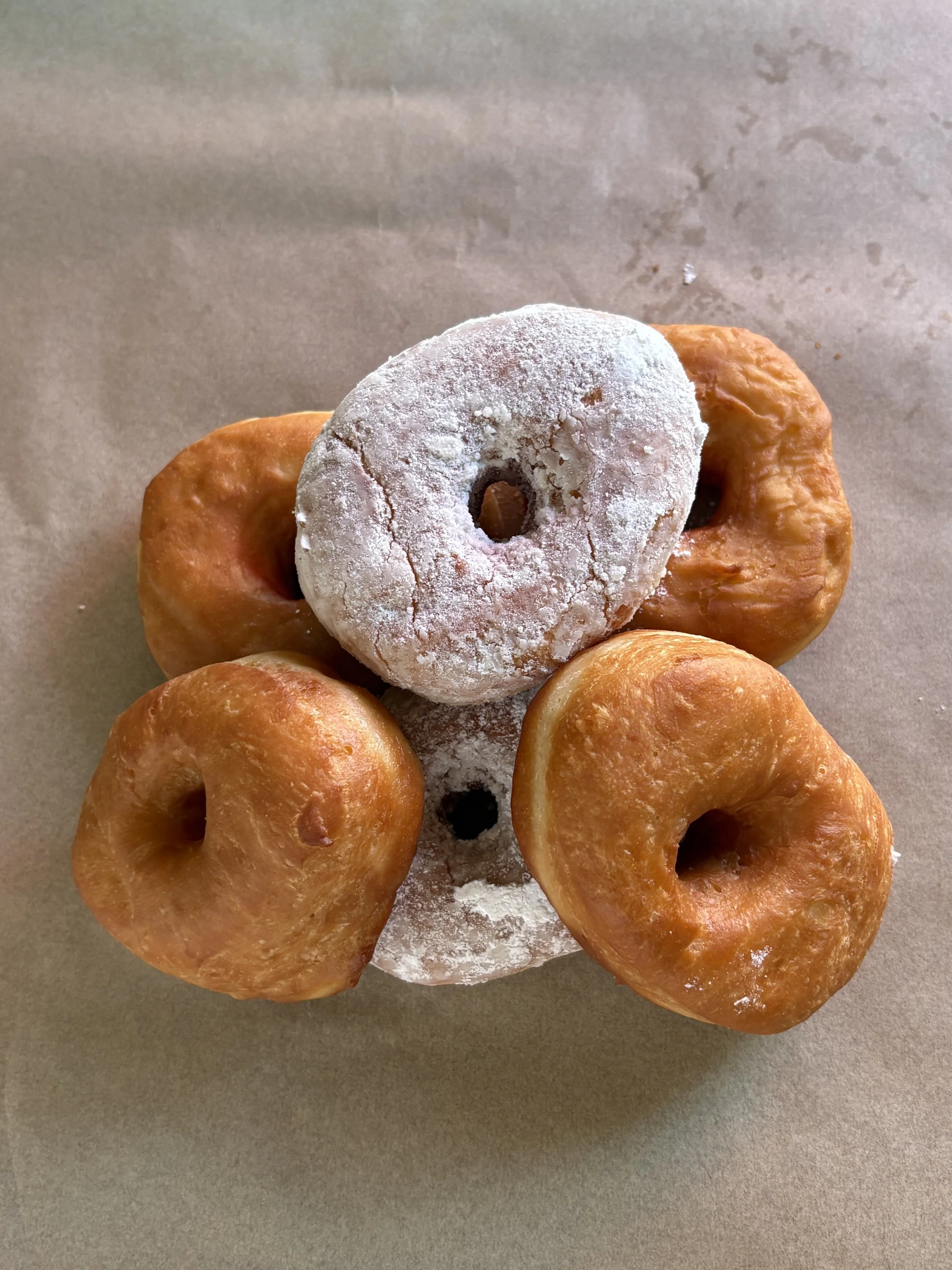 Six glazed doughnuts, one powdered sugar doughnut in the center, arranged on a flat surface.