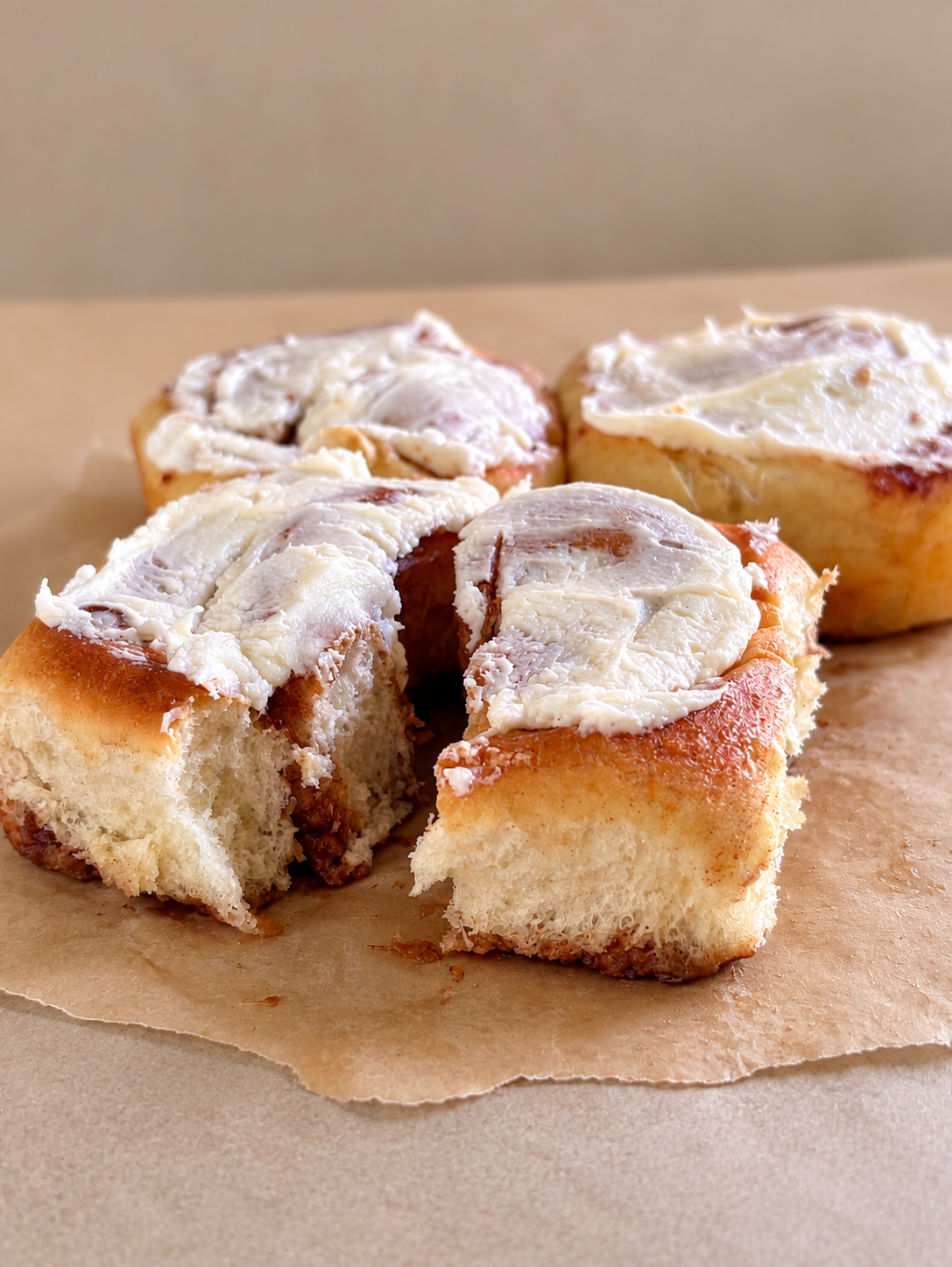 Three cinnamon rolls with white icing on top, one broken into, placed on brown parchment paper.