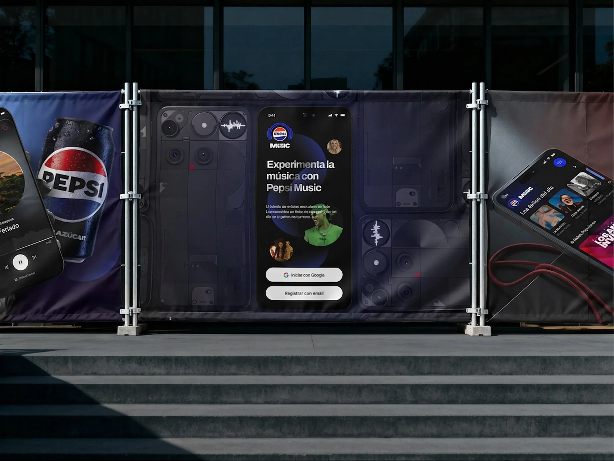 Pancarta publicitaria con promoción para experimentar música con Pepsi Music, mostrando un teléfono móvil con la app abierta y un cartel con el logo de Pepsi, en un espacio exterior con fondo de vidrio oscuro.