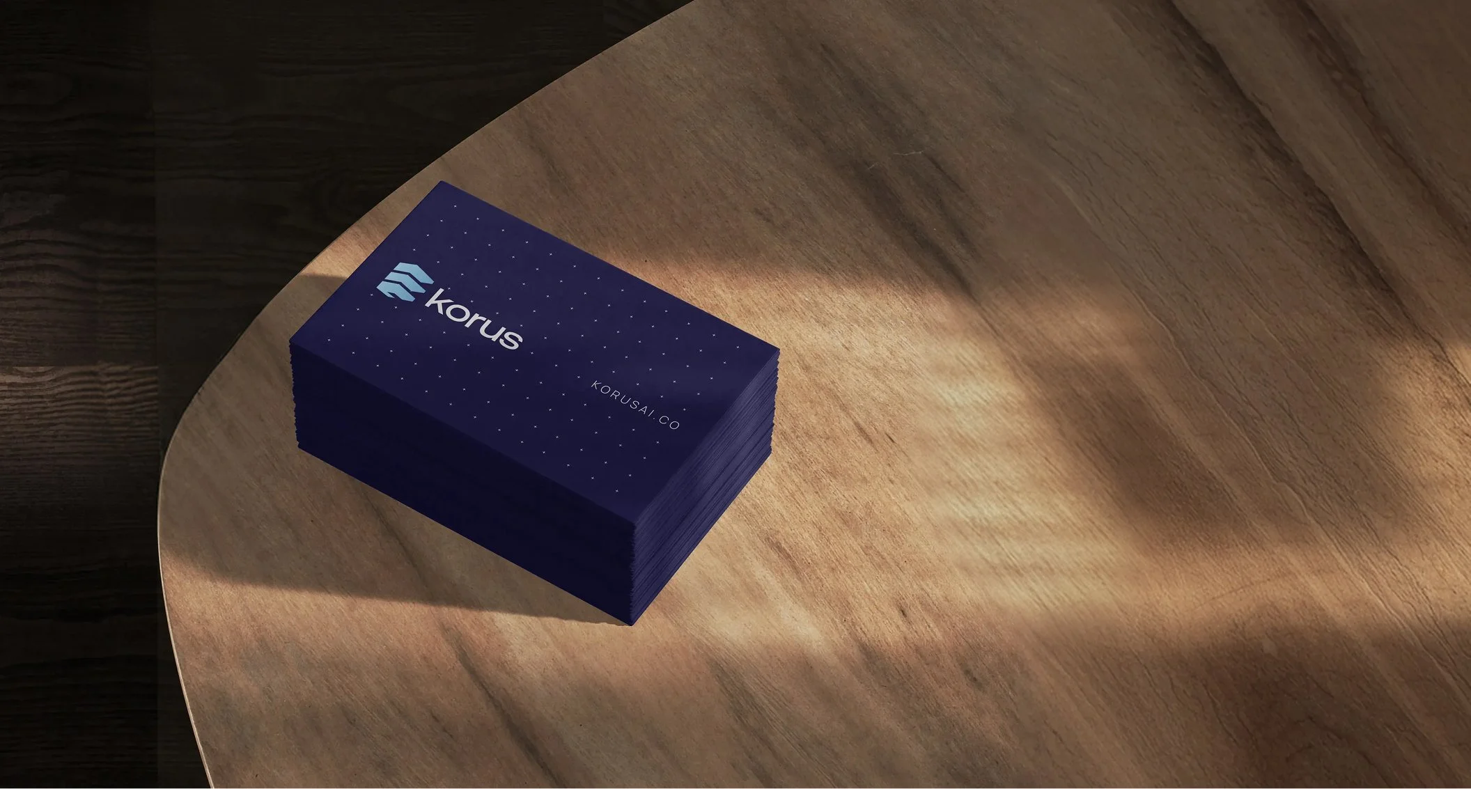 Una pila de tarjetas de visita de color azul con el logotipo y el nombre 'Korus' sobre una mesa de madera redonda.