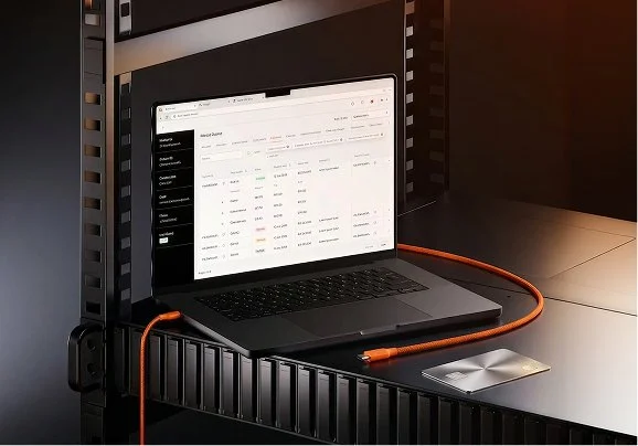 Portátil en un estante con pantalla que muestra una interfaz de datos, conectado a un disco duro externo con un cable naranja.