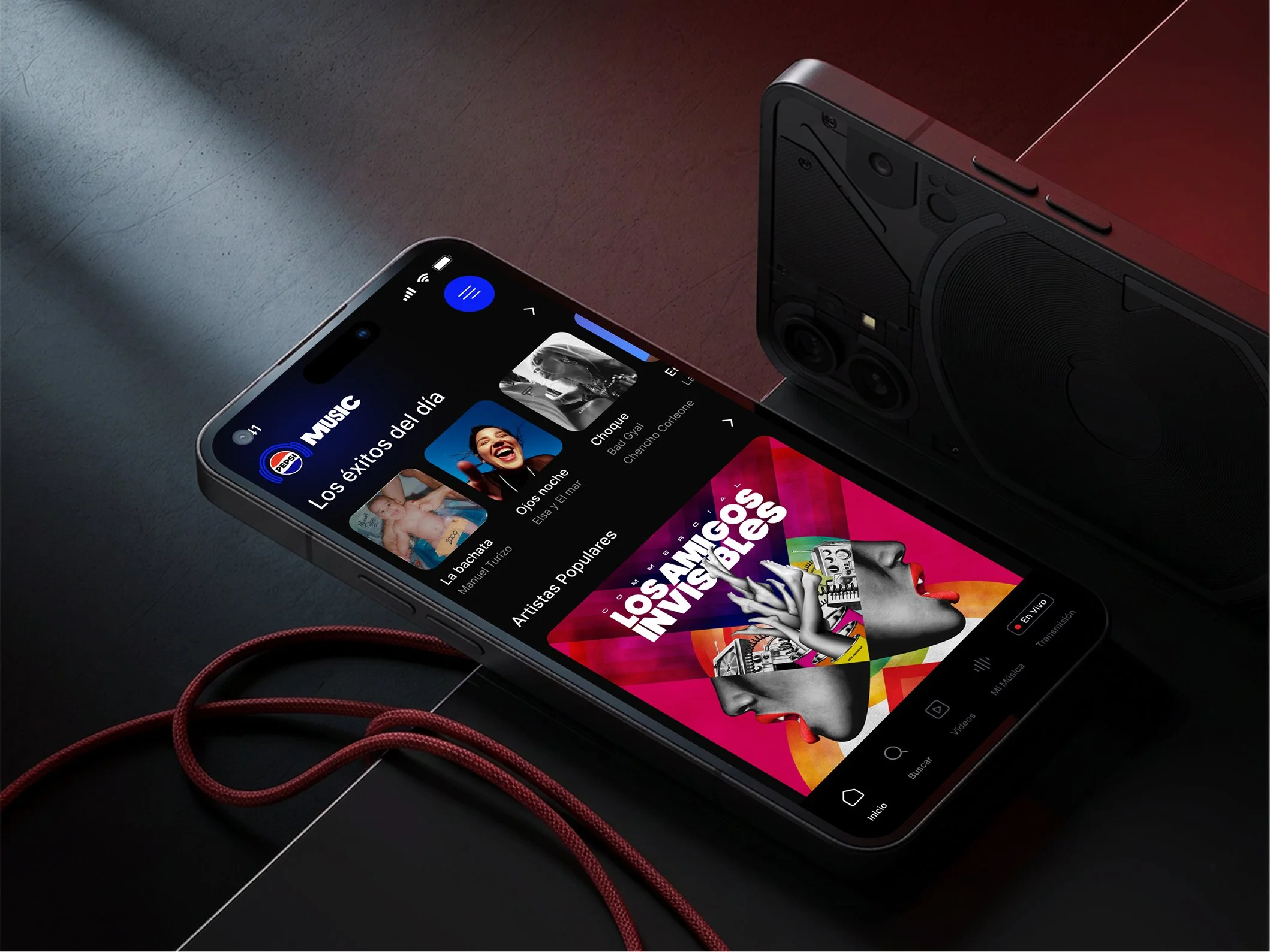 Un teléfono inteligente mostrando una lista de música en pantalla, conectado por unos auriculares de diadema rojos, con un parlante grande en el fondo sobre una superficie de color oscuro.