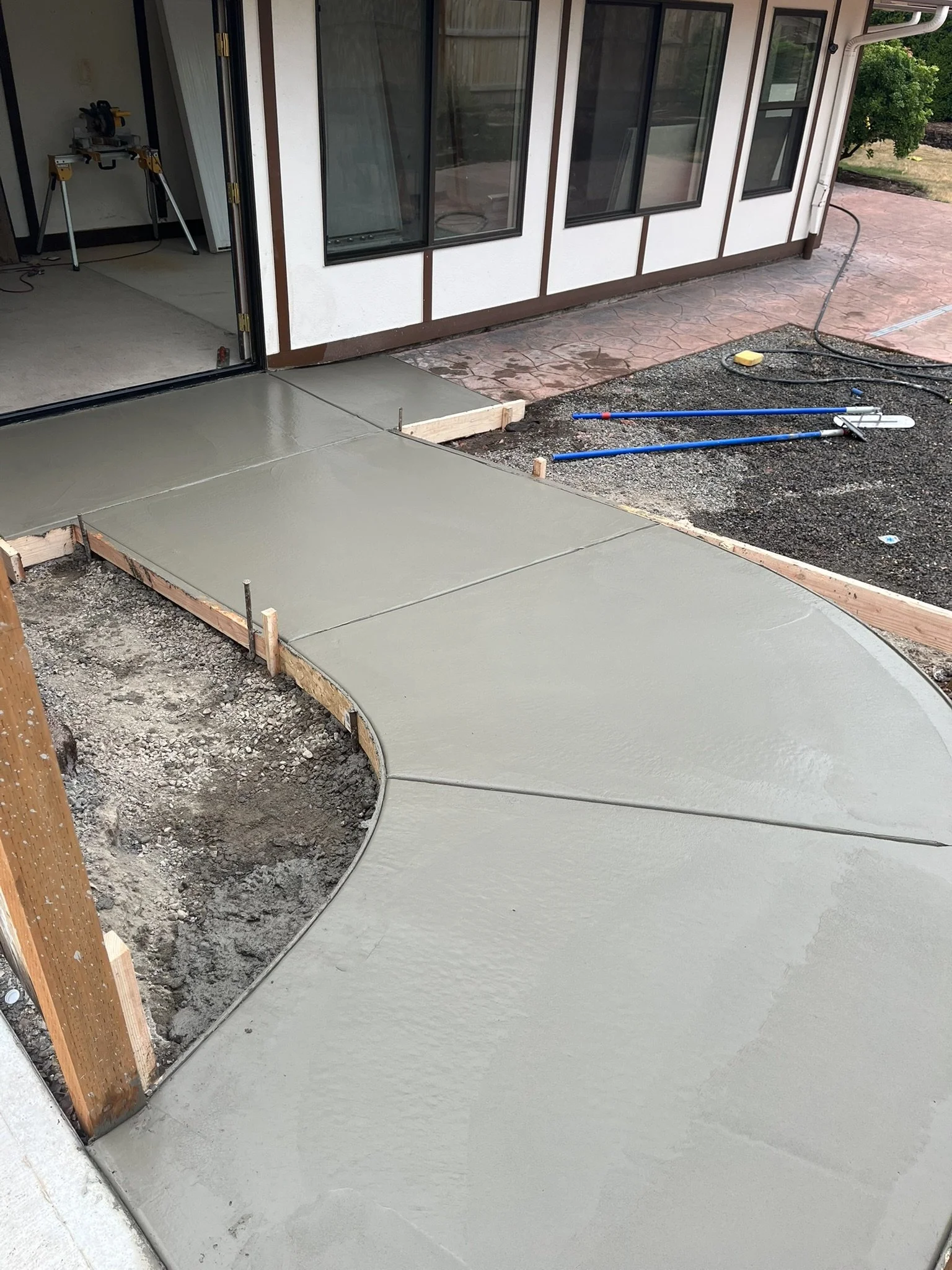 Fresh concrete walkway with curved edges and wooden forms beside a house.