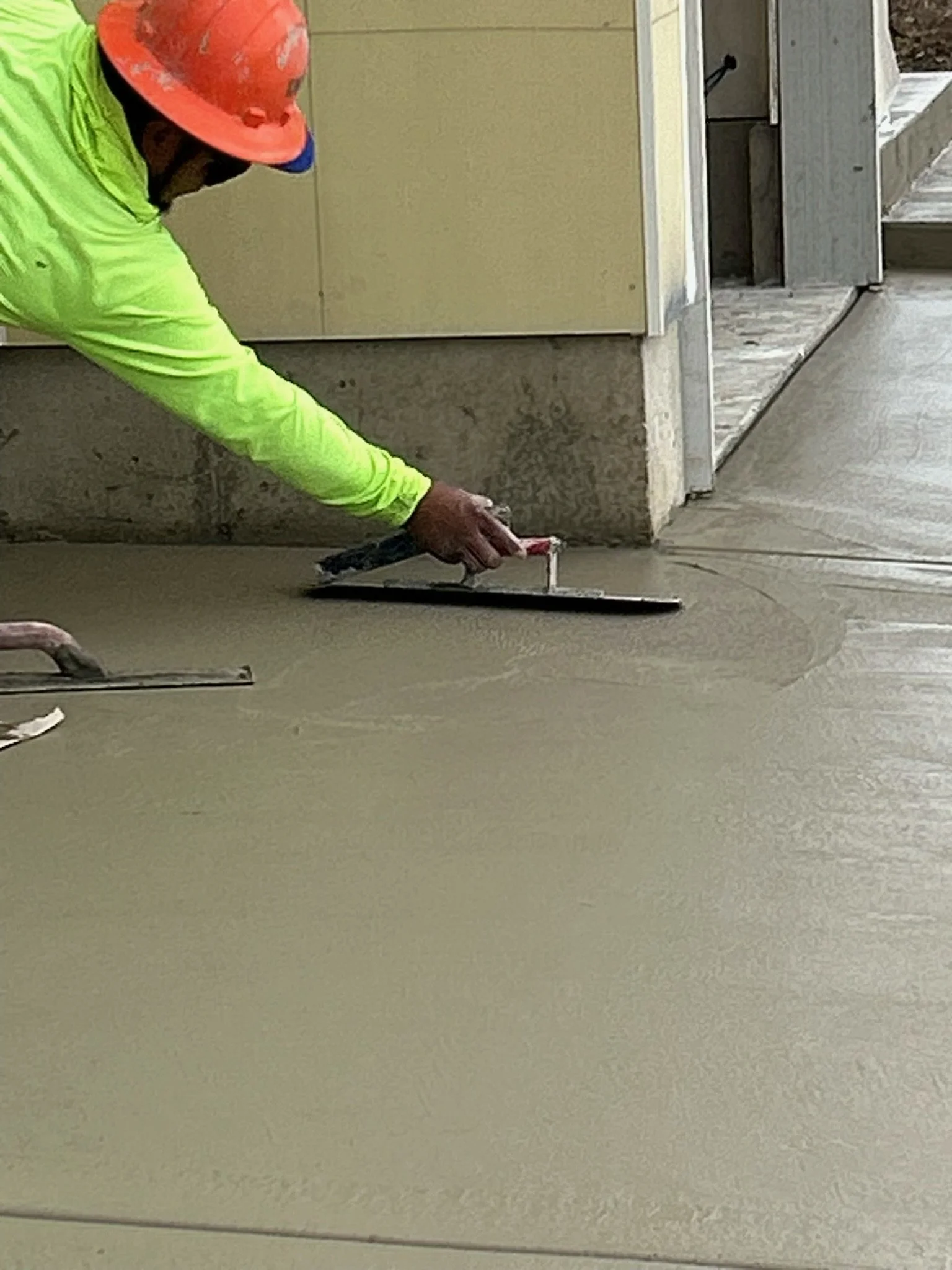 Concrete finisher smoothing a fresh surface with a hand trowel.