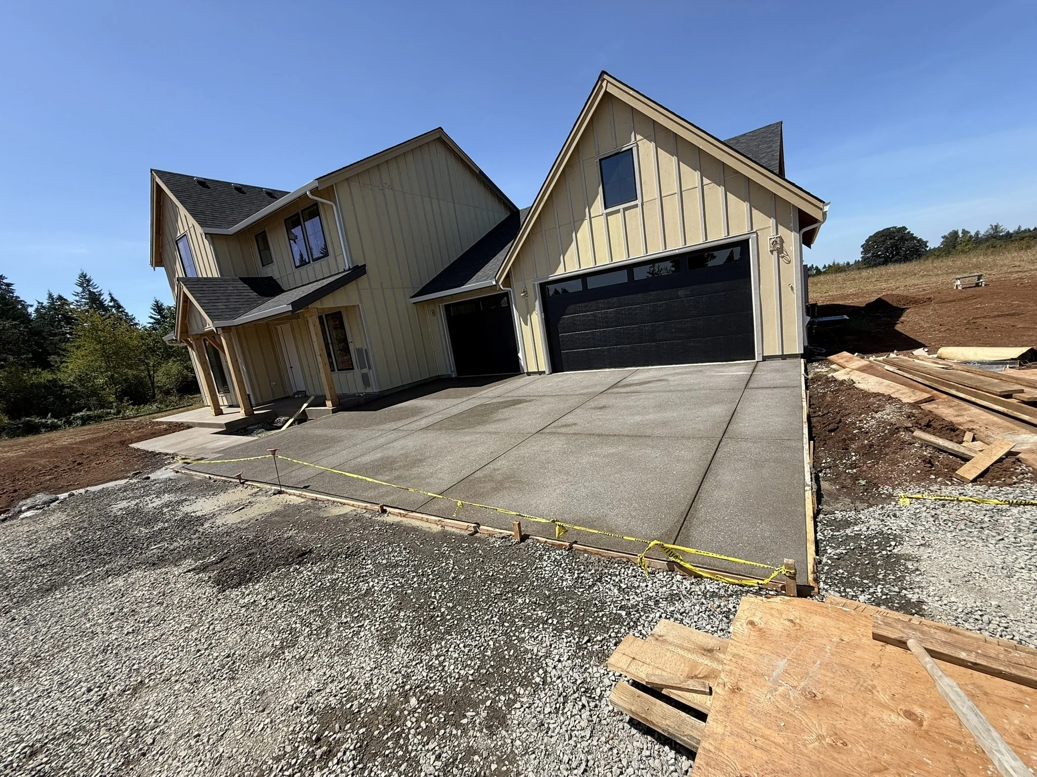 New concrete driveway in front of a garage, with temporary forms and caution tape.