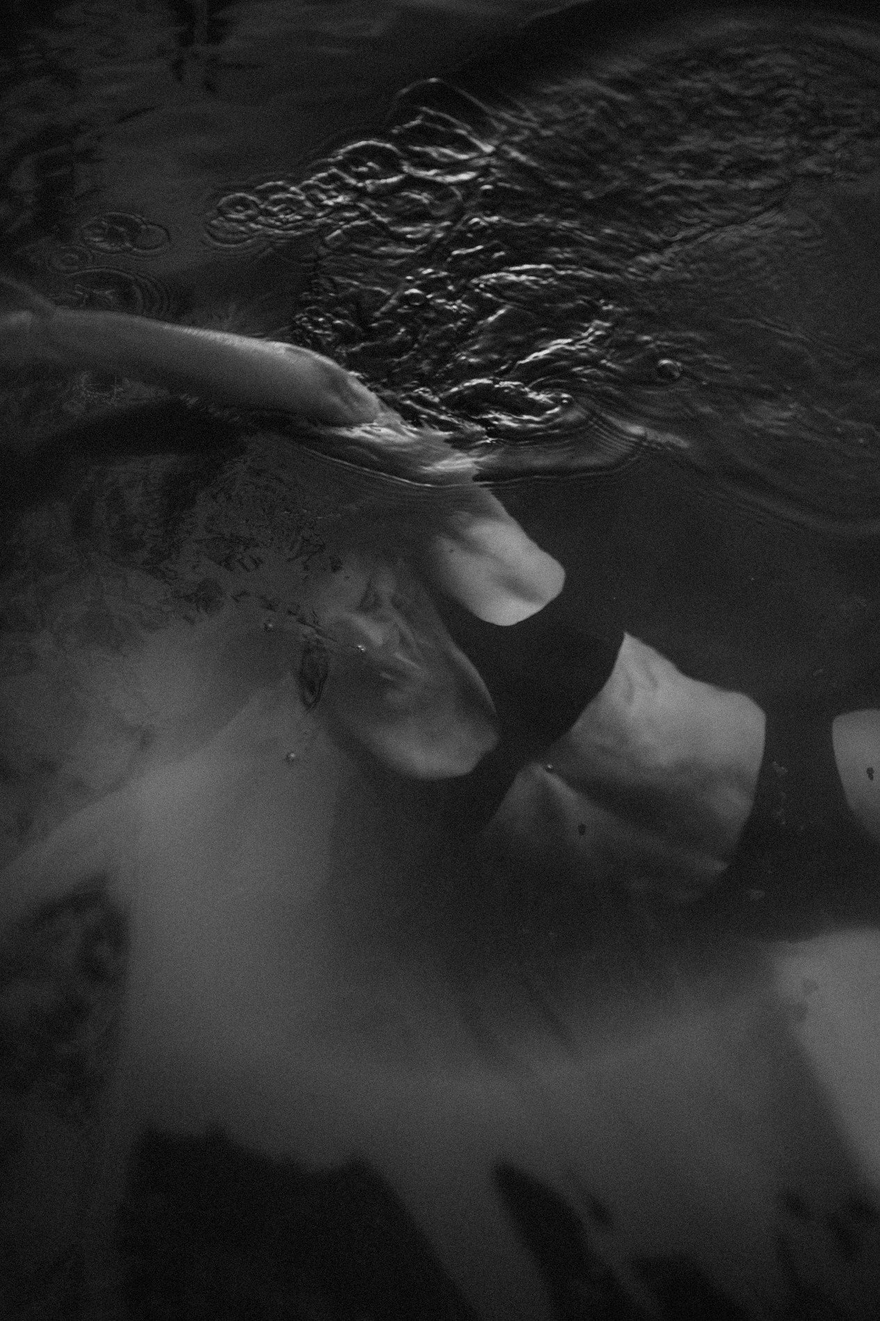 Cuerpo de una persona en el agua, parcialmente sumergido, en un entorno oscuro.