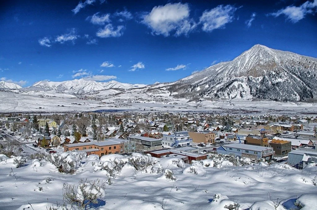 Snow-covered small town Crested Butte, Colorado with colorful buildings in a valley surrounded by mountains on a clear, sunny day.