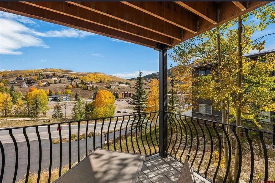 Mountain view from a balcony with trees in fall colors and a parking lot below