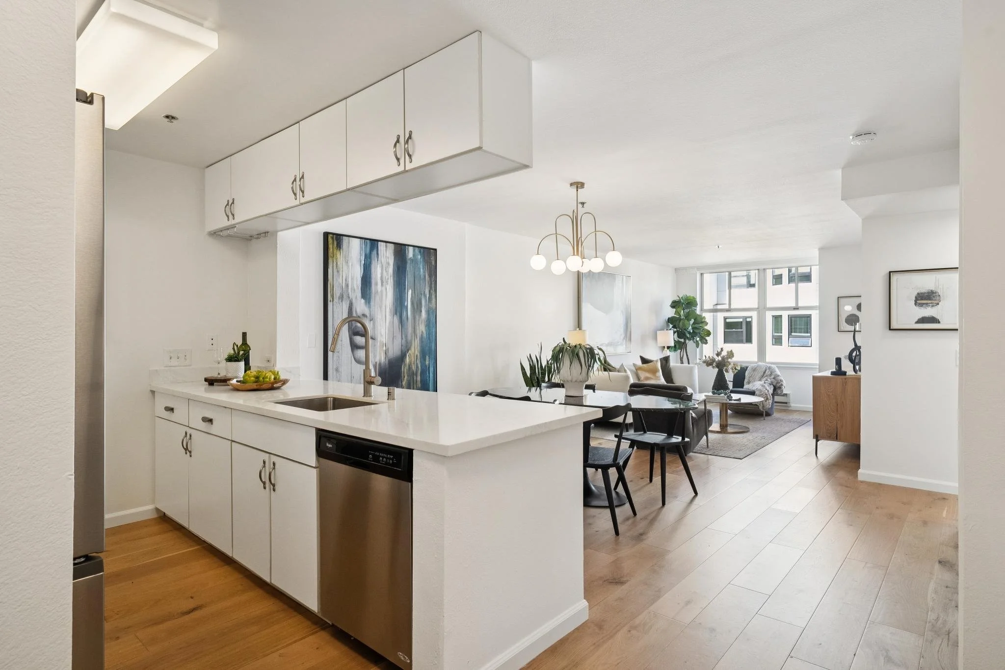 Open floor plan living room and kitchen with white cabinets, a chandelier, large windows, and modern decor.