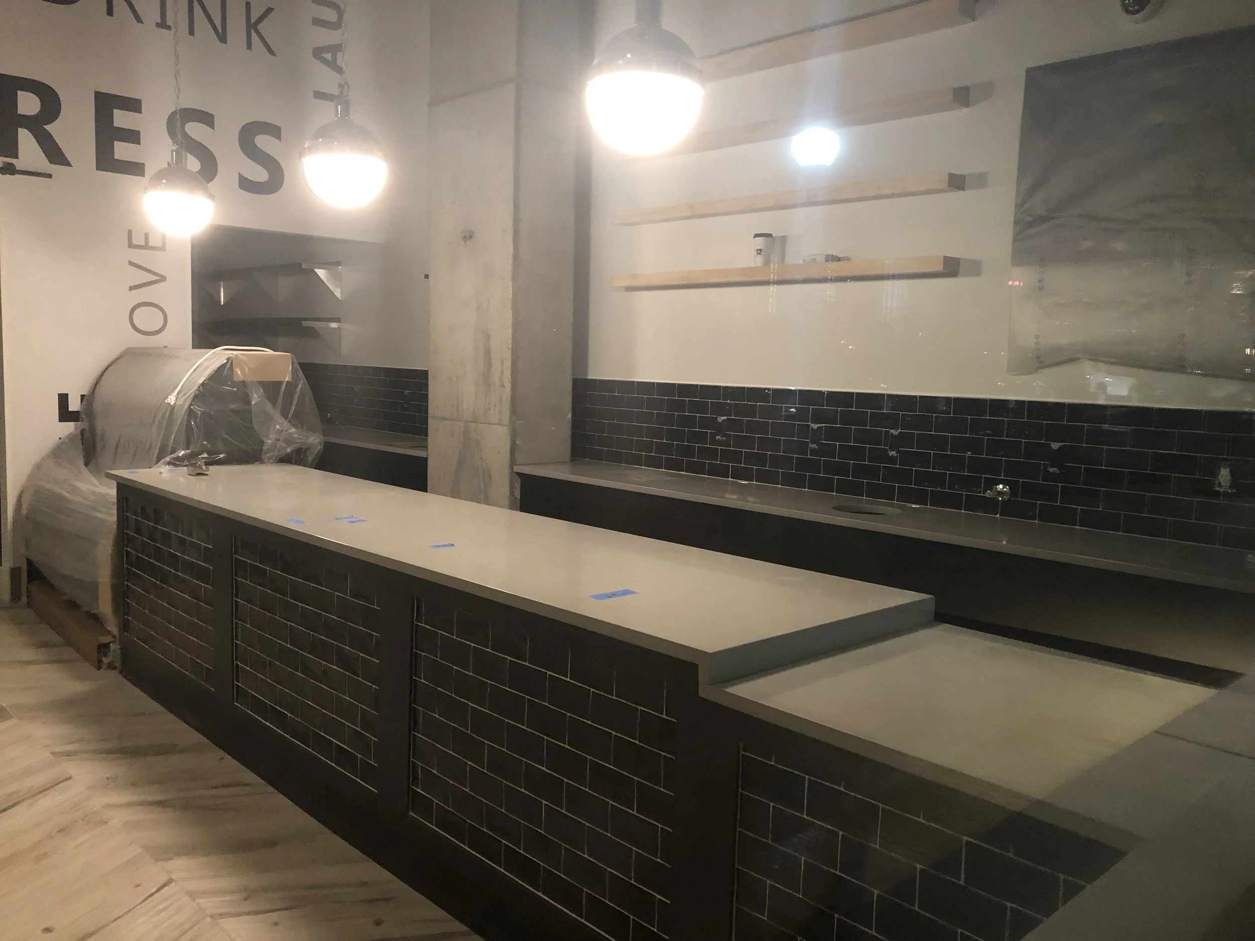 Empty coffee shop or restaurant counter with black subway tile, wooden shelves, and hanging light fixtures.