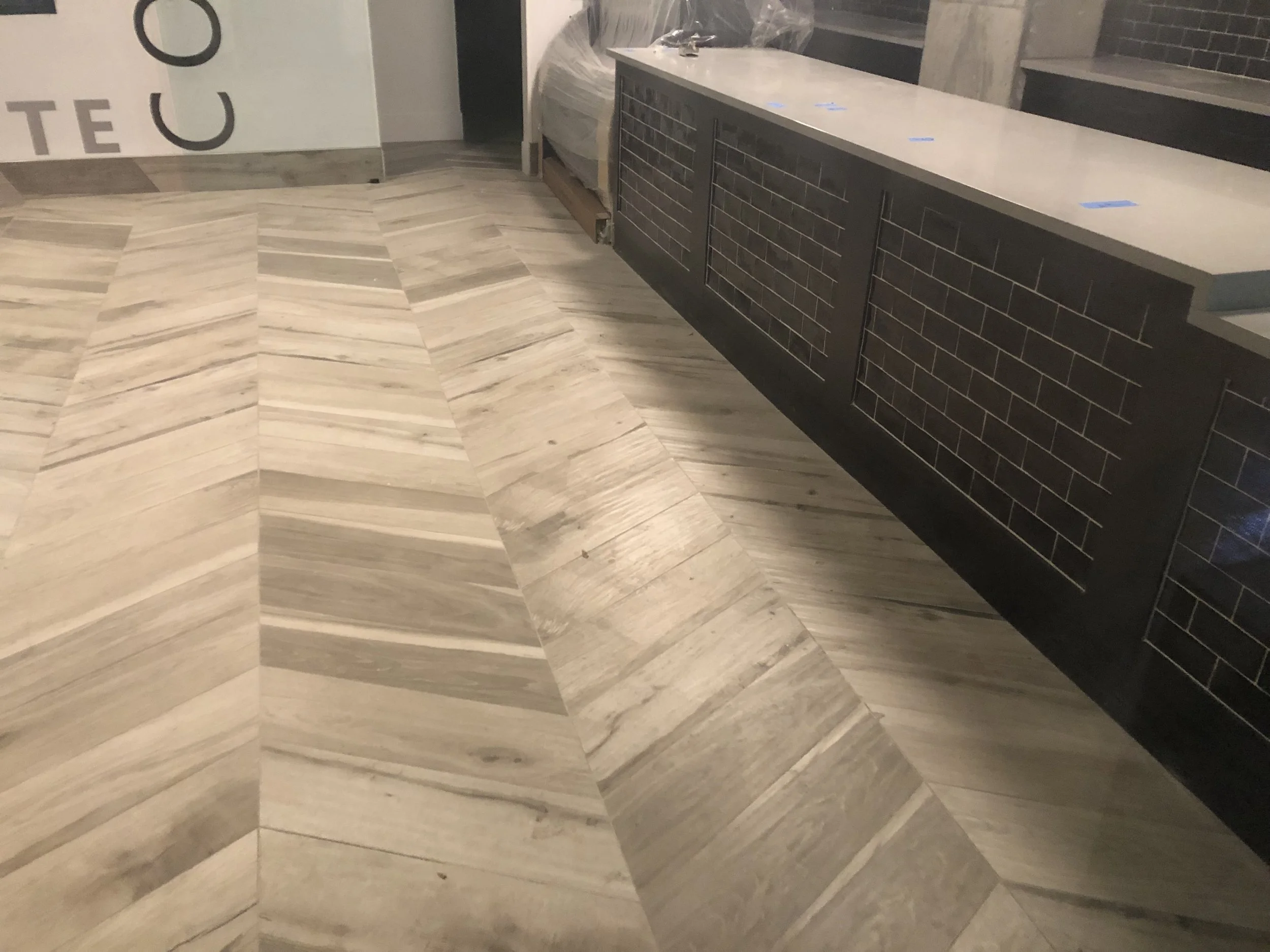 Interior of a building under construction with a black brick wall, a white marble countertop, and a tiled wooden floor with a chevron pattern.
