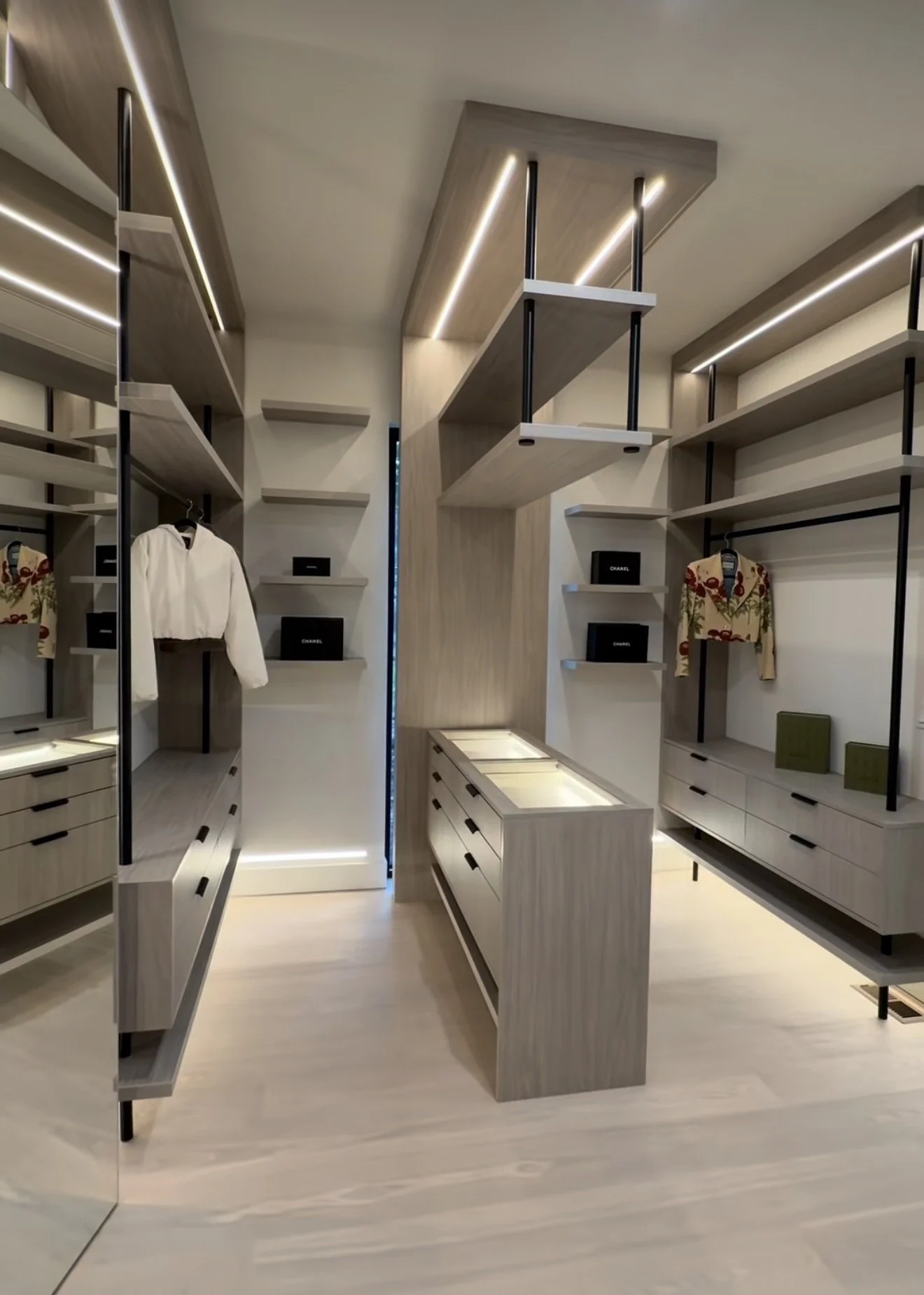 Modern walk-in closet with built-in shelves, drawers, clothing, and accessories display, illuminated with built-in lighting.