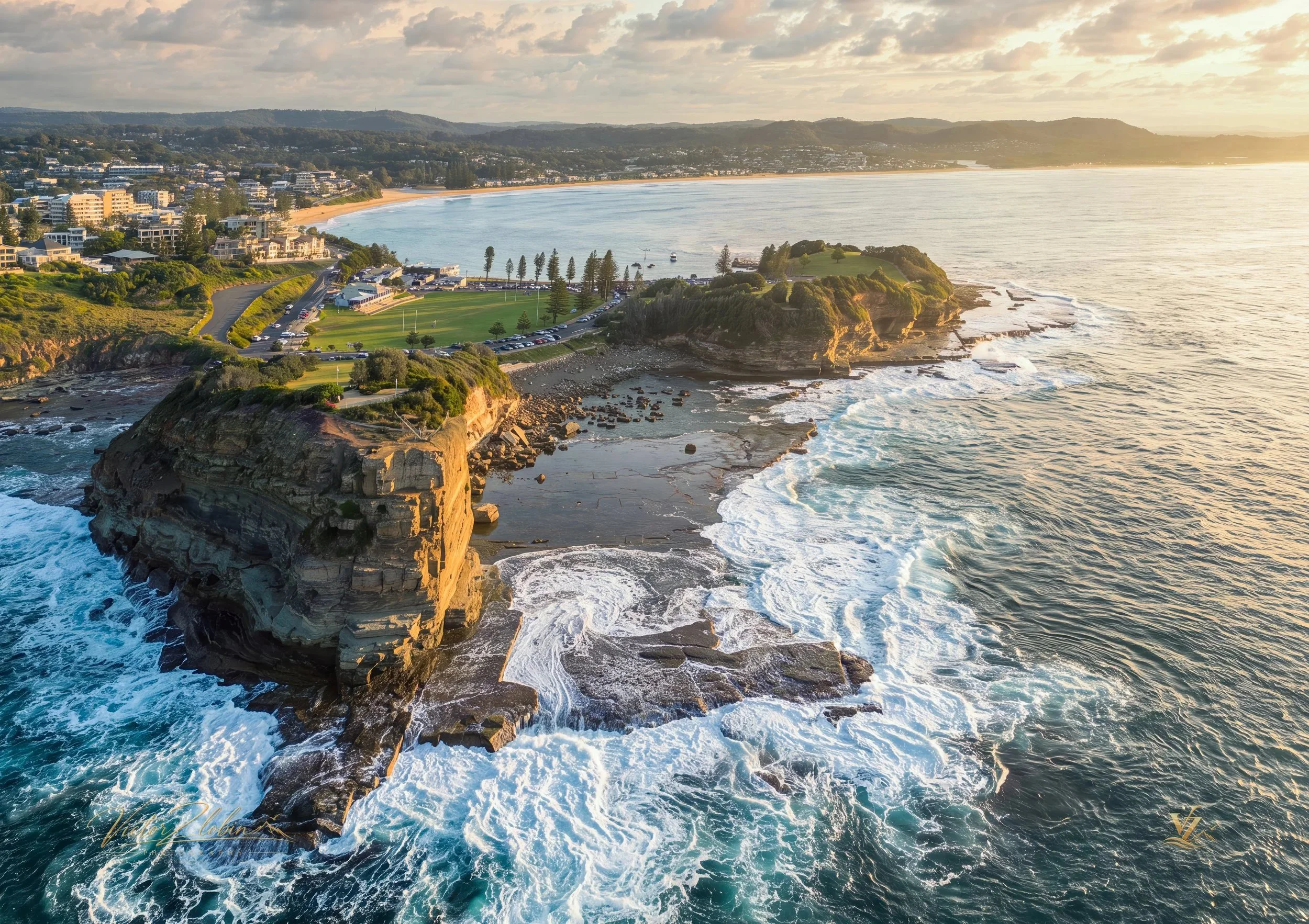 Aerial view of Terrigal Headland with The Skillion rising above the rugged coastline. Powerful ocean waves sweep across the rock platforms as the evening sun casts warm golden light over Terrigal Beach and the Central Coast landscape. 0705