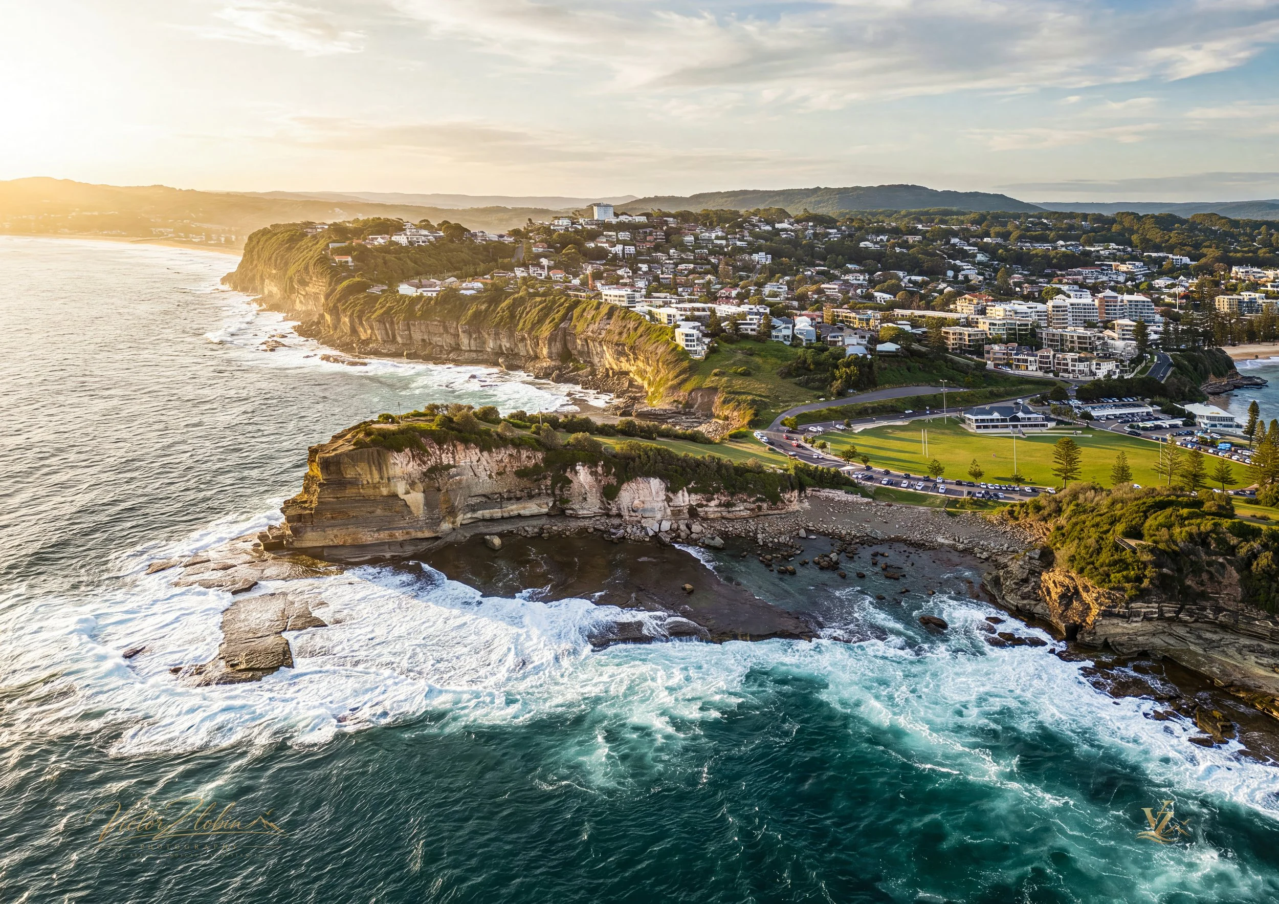 Aerial photograph of Terrigal Headland and The Skillion on the NSW Central Coast, revealing dramatic sandstone cliffs, rugged rock platforms and powerful ocean waves in warm early-morning light. 0750
