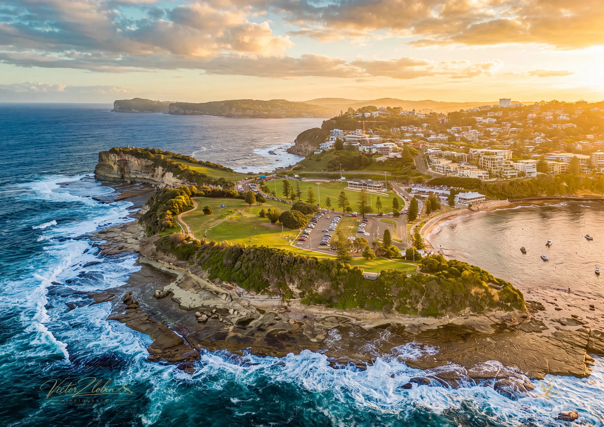 Aerial photograph of The Skillion at Terrigal Headland on the NSW Central Coast, illuminated by sunrise
 light, with dramatic coastal cliffs, rock platforms, ocean waves, Terrigal Beach and the surrounding coastline. 0722