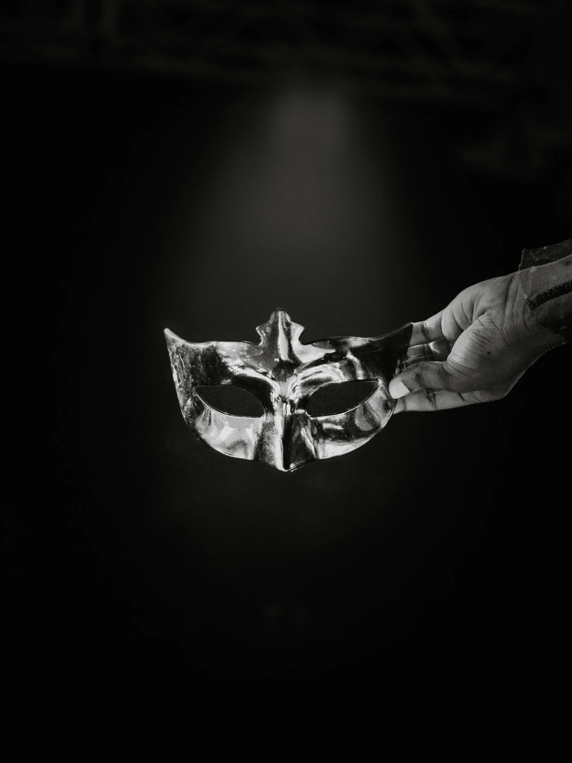 A hand holding a silver skull-shaped object against a dark background.